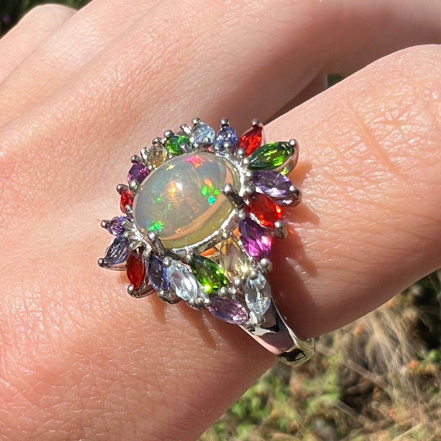An Ethiopian opal and gemstone-accented ring worn on a finger at an angle in natural sunlight.