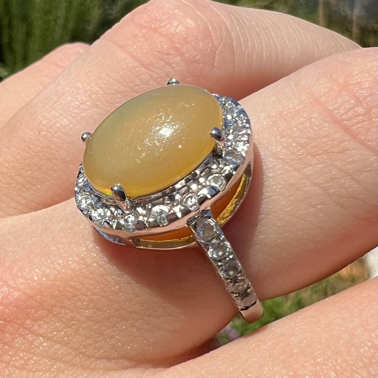 Close-up of a finger wearing a sterling silver Ethiopian fire opal ring with a CZ halo, shown at an angled view.