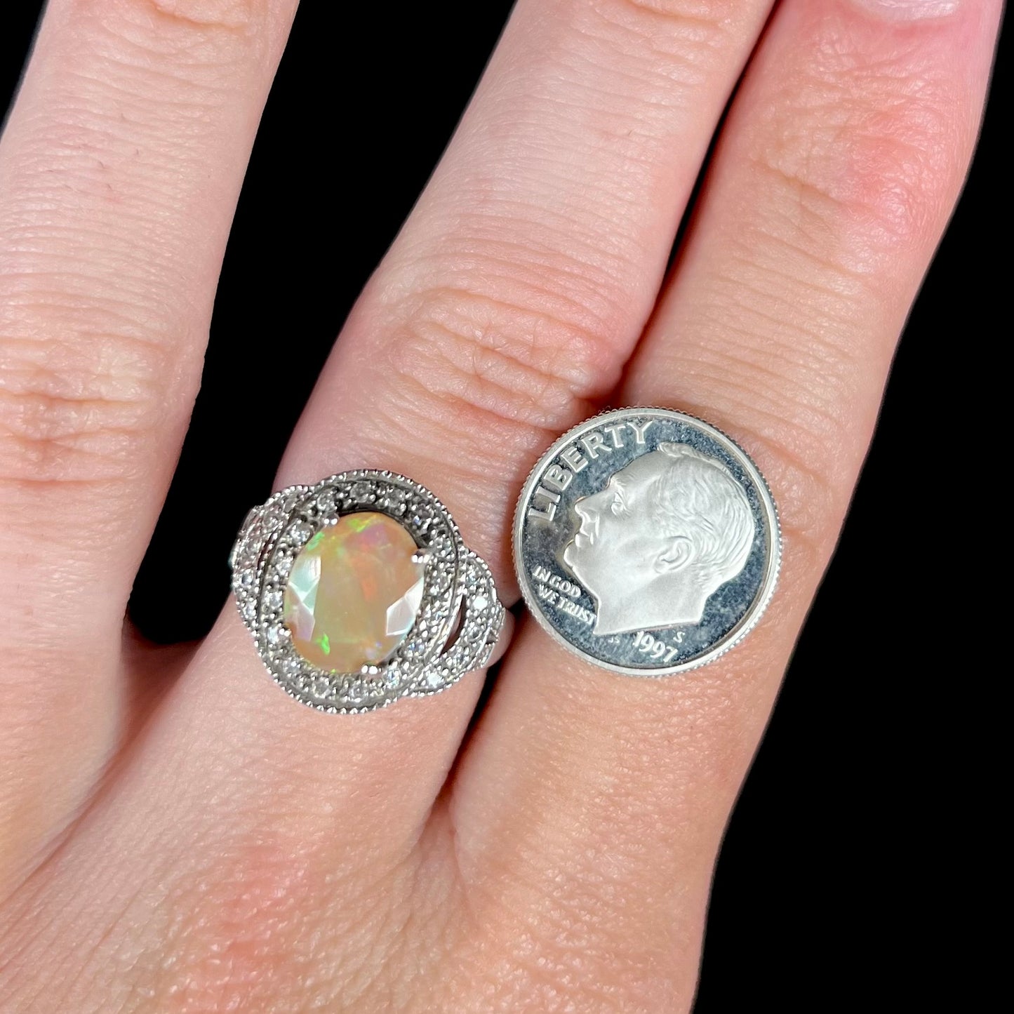A silver Ethiopian opal halo ring worn on a finger next to a dime coin.