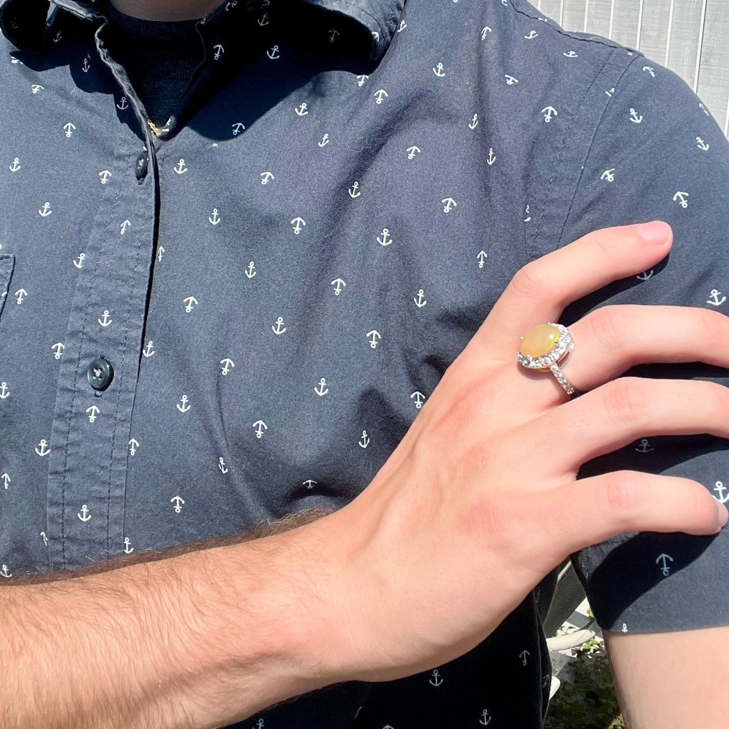 A sterling silver Ethiopian fire opal ring with a CZ halo worn on a hand as it rests on the model's opposing shoulder.
