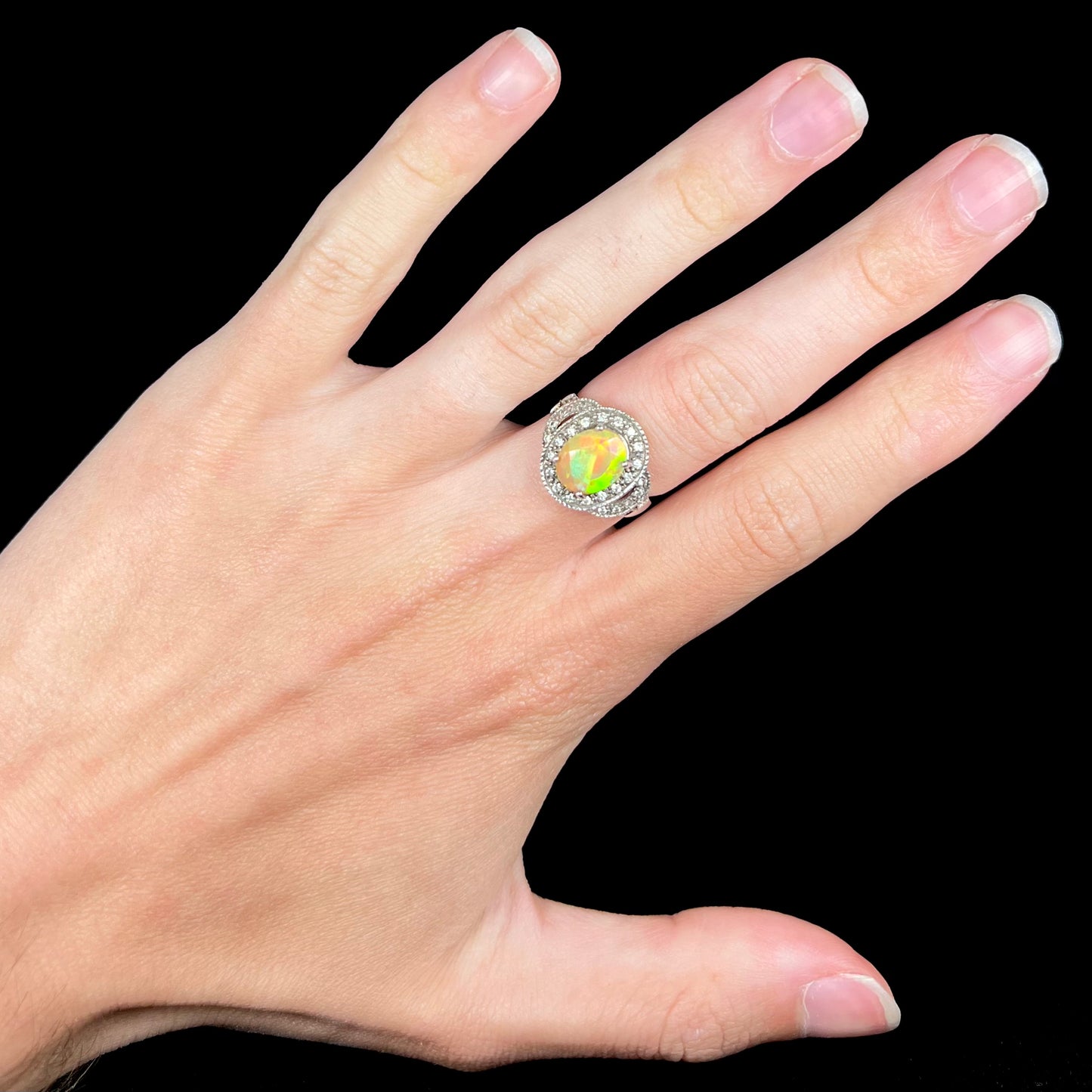 An Ethiopian opal and CZ halo ring worn on a hand. The oval shaped opal shows green flashes of color.