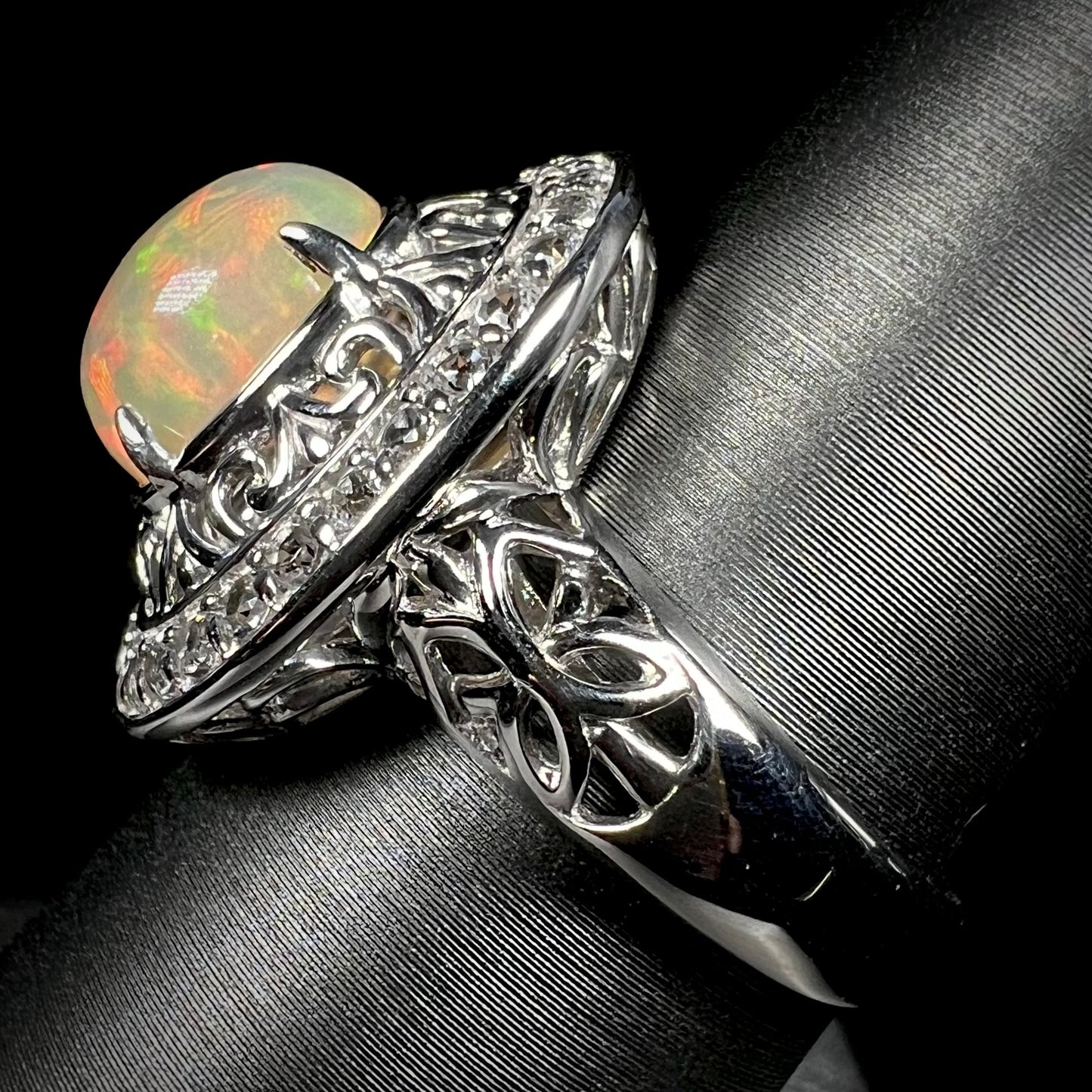 Side view of silver Ethiopian opal filigree halo ring against black background.