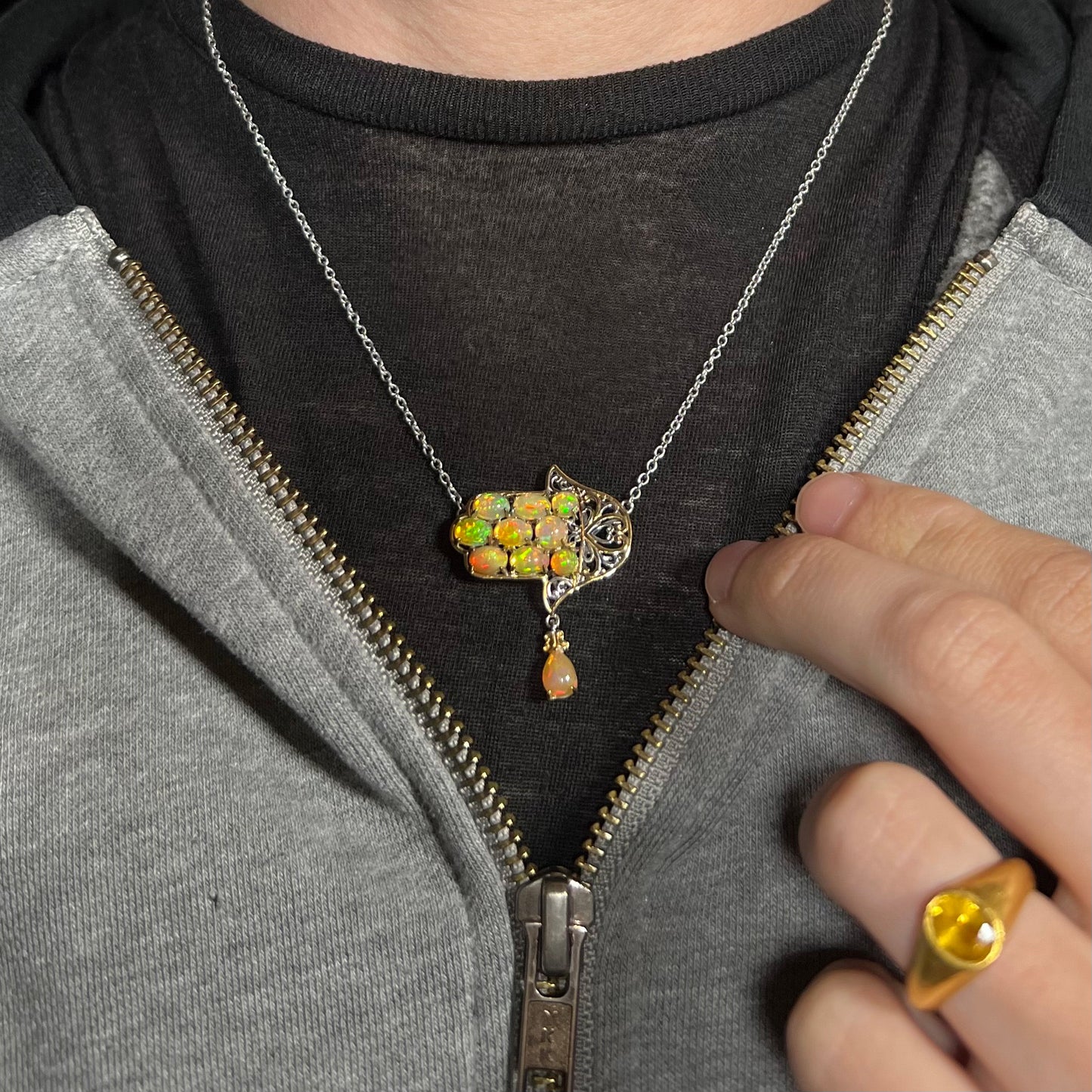 An Ethiopian opal hamsa necklace, worn around a neck against a dark shirt and partially zipped hoodie.