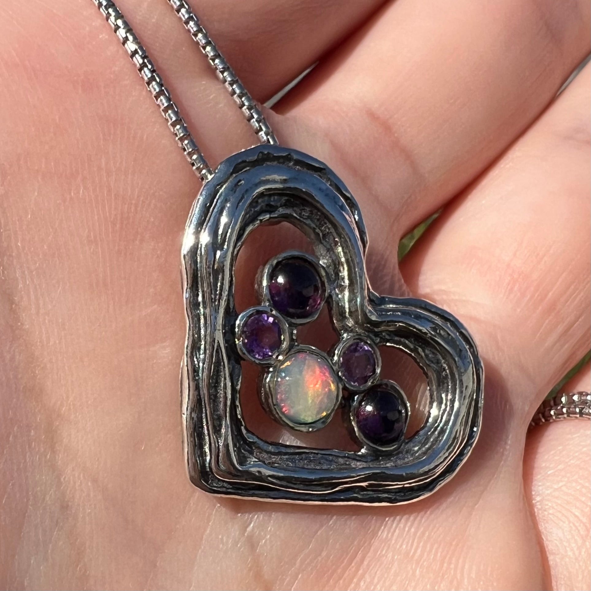 A sterling silver heart necklace set with a round Ethiopoian opal, two amethysts, and two rhodolite garnets.