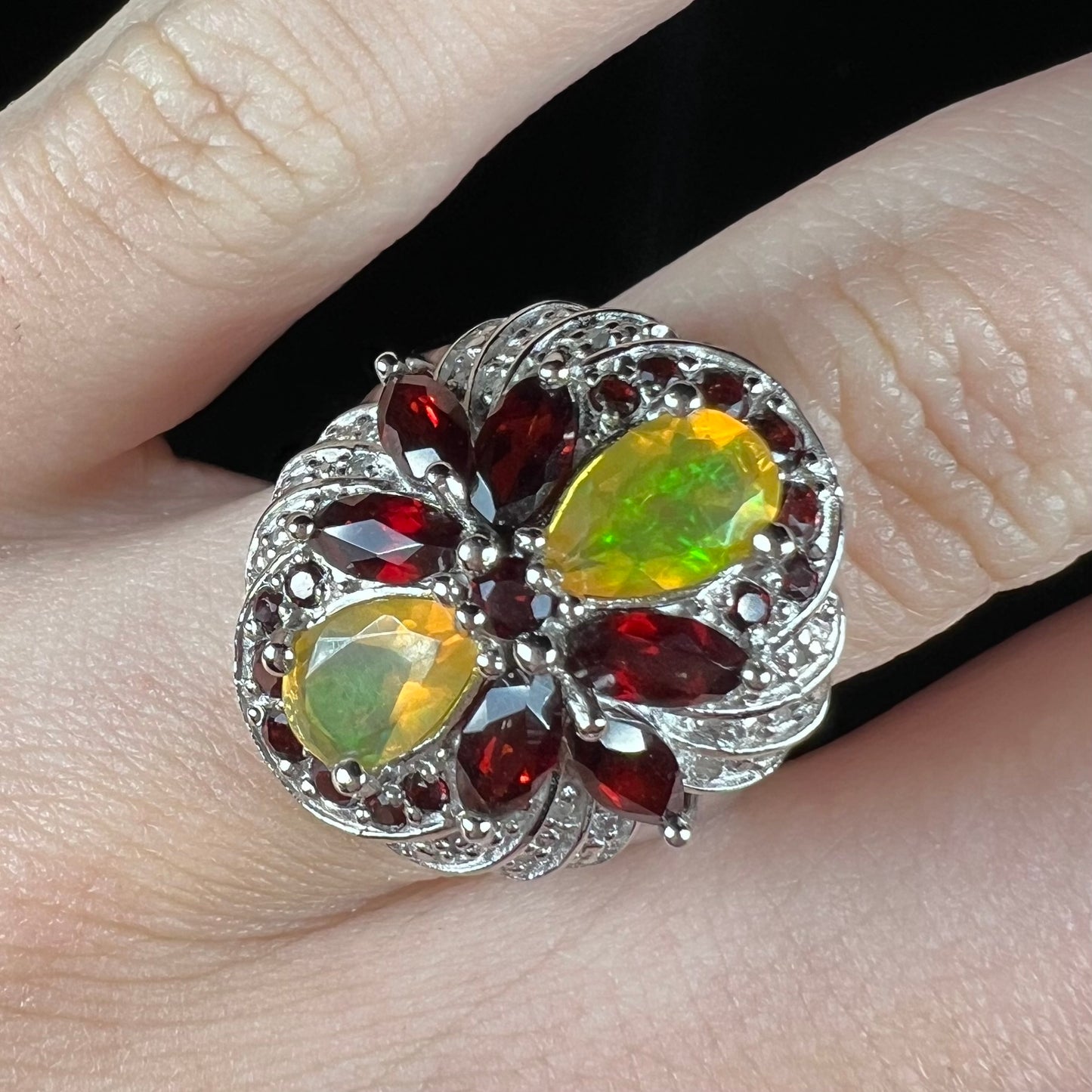 An Ethiopian opal infinity ring with garnet and diamond accents, worn on a finger.