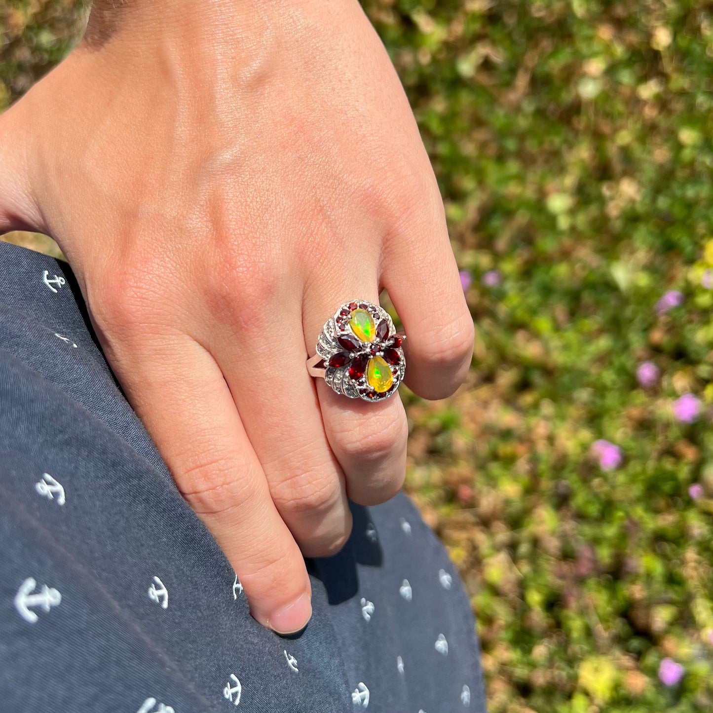 An Ethiopian opal infinity ring worn on a hand as it rests on the model's hip in natural sunlight.