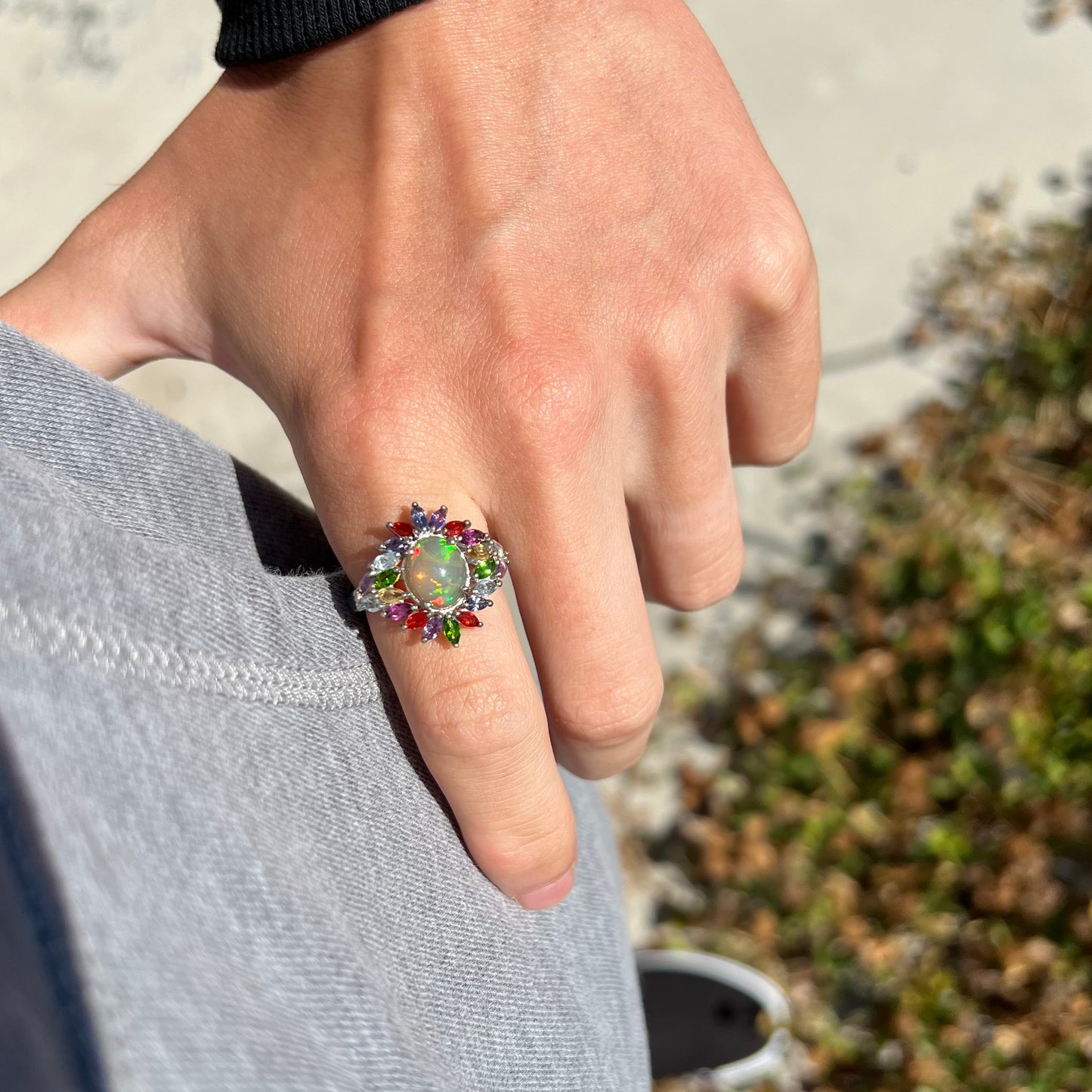 An Ethiopian opal and multi-gemstone ring worn on a hand as it rests on a hip in natural outdoor light.