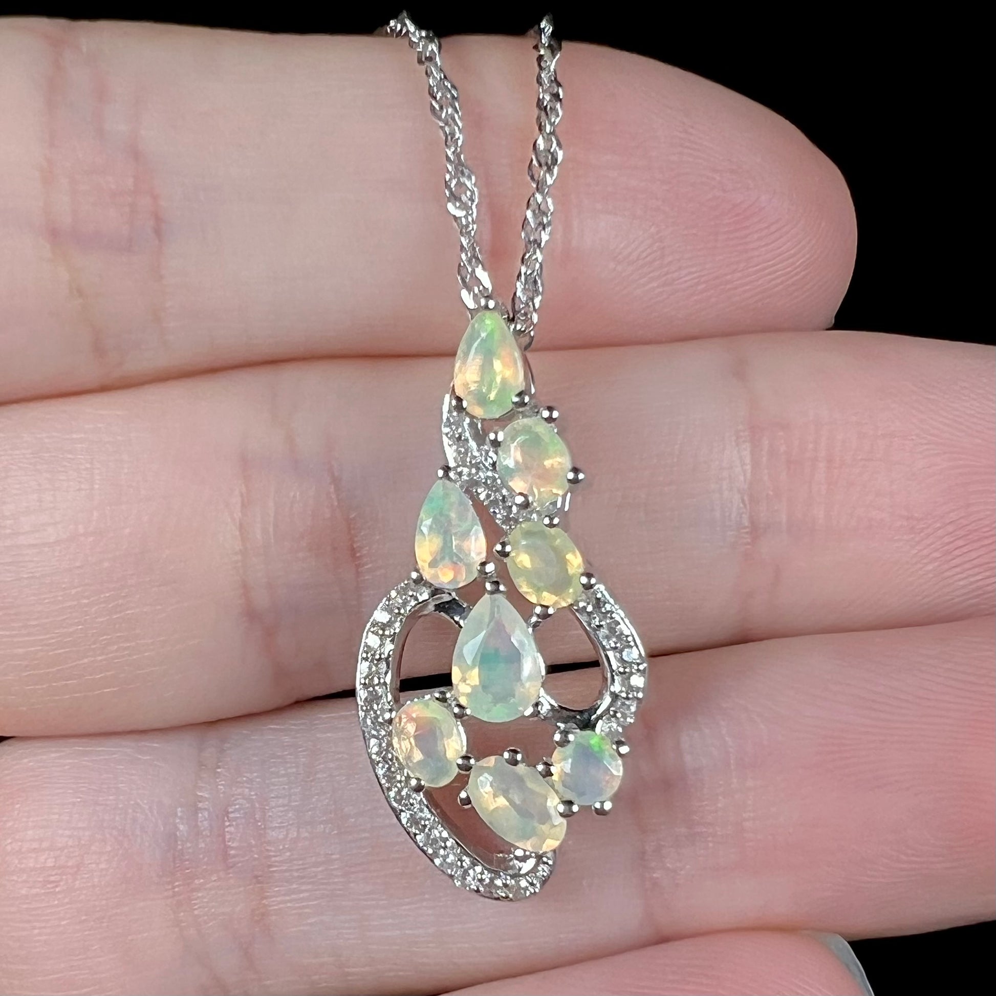 A silver Ethiopan opal and cubic zirconia necklace, shown close-up in a hand.