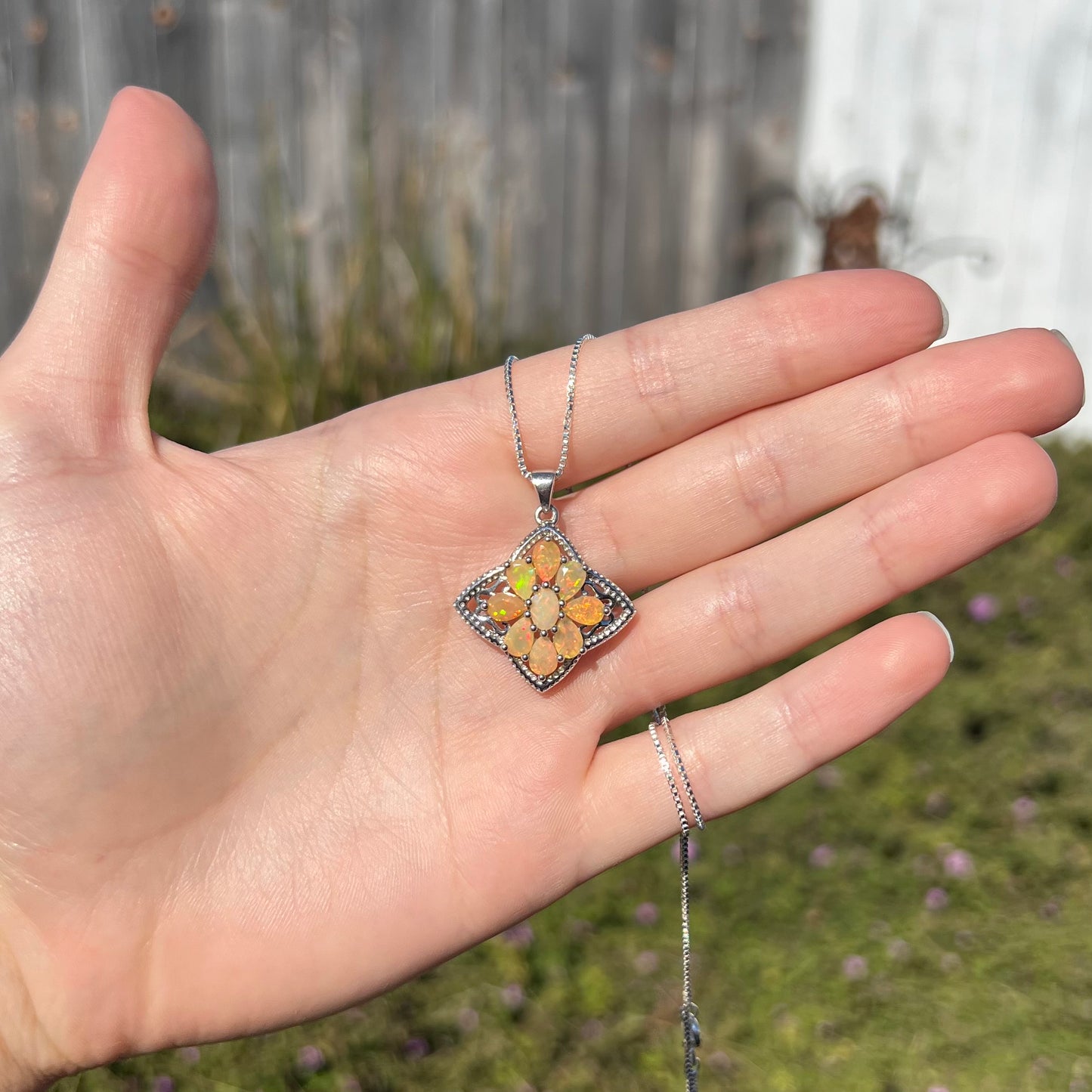 An Ethiopian opal star necklace made from sterling silver shown in the sunlight, held in a hand.