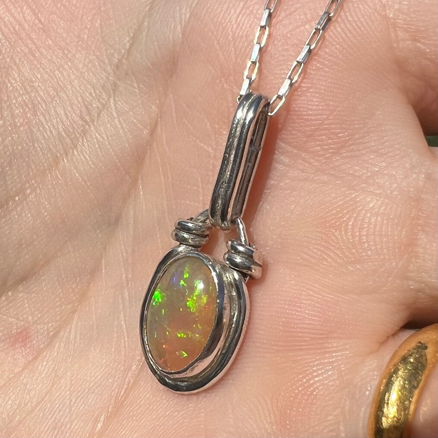 A colorful sterling silver Ethiopian opal pendant shown close-up from an angle in the sunlight against a hand.