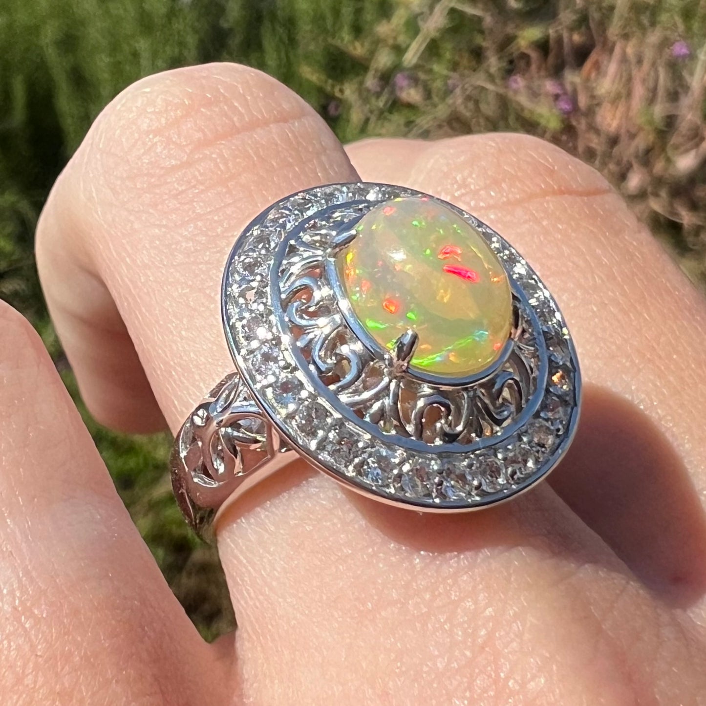 A sterling silver Ethiopian opal halo ring with a double halo of filigree and white topaz accents in the sunlight.