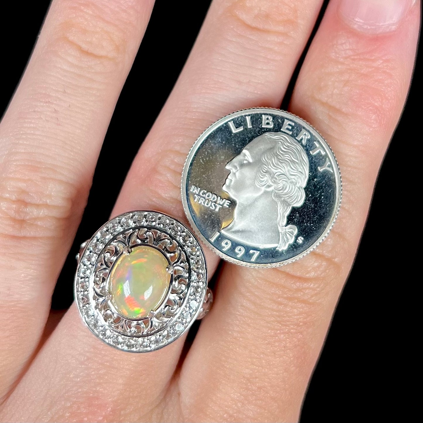 A silver Ethiopian opal halo ring next to a quarter.