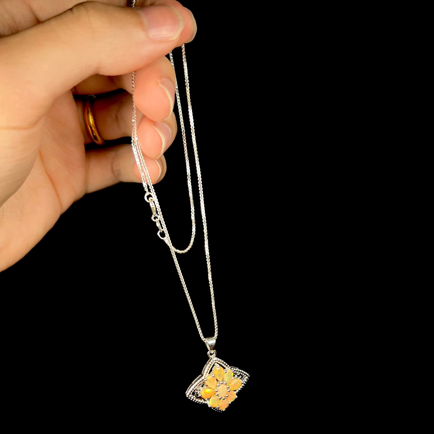 A sterling silver Ethiopian opal star necklace held in a hand, dangling by its box-style chain.