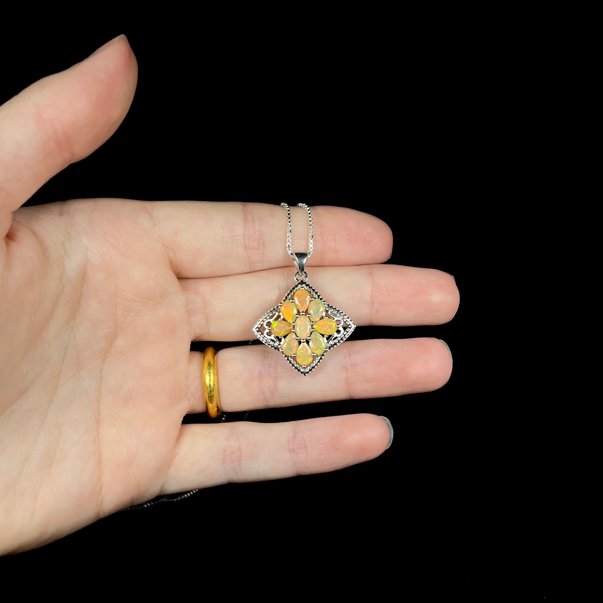An Ethiopian opal cluster star necklace made from sterling silver, shown in a hand against a black backdrop.
