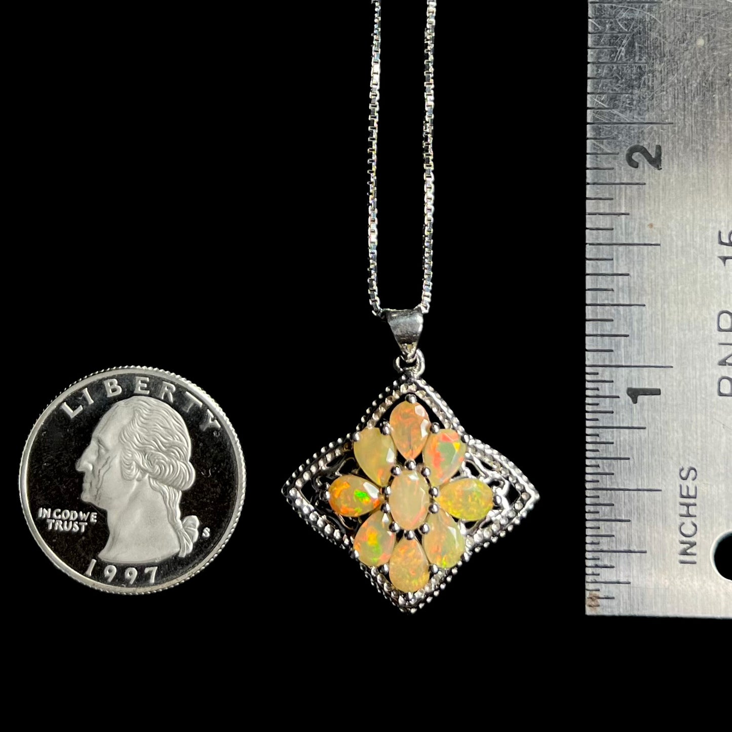 A silver Ethiopian opal star necklace shown next to a quarter coin and ruler.  The pendant measures 1.25 inches long.