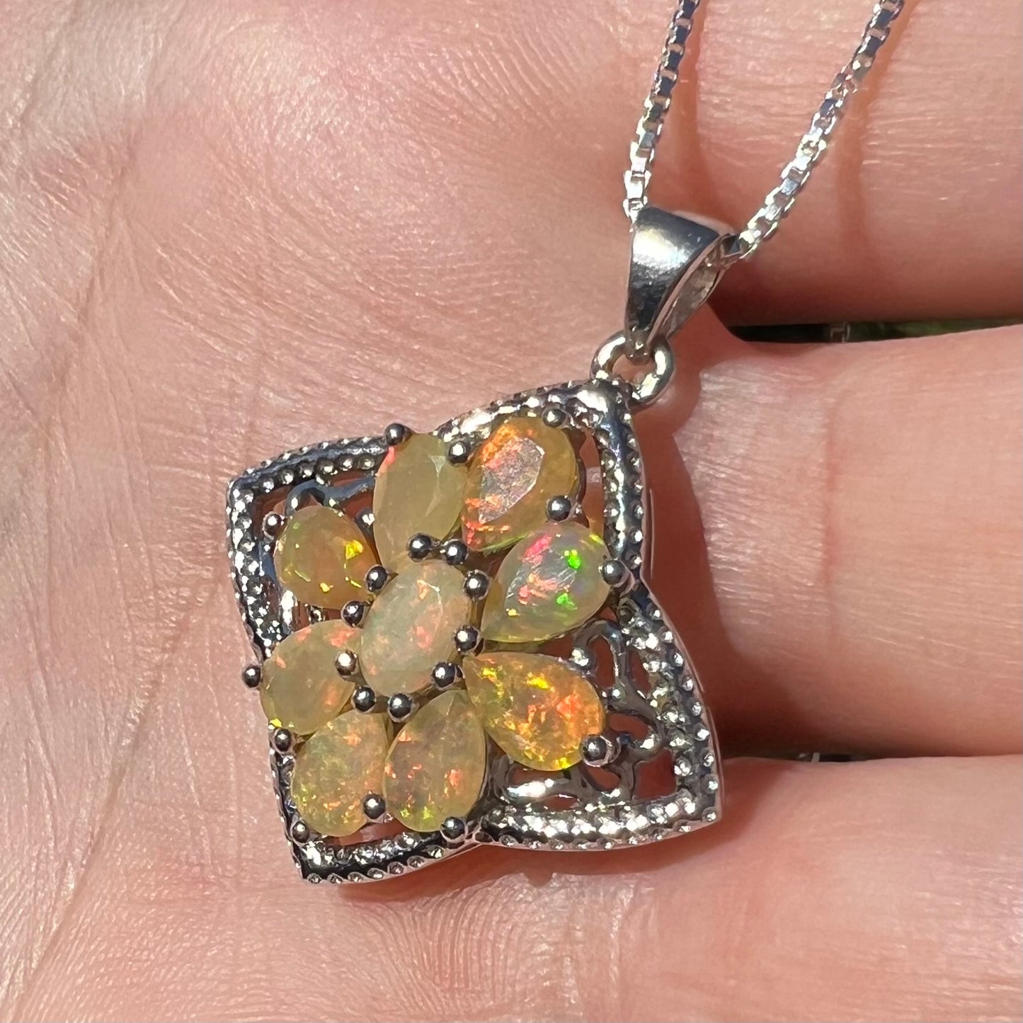An Ethiopian opal star necklace shown in the sunlight in a hand at an angle.  The opals have orange color play.