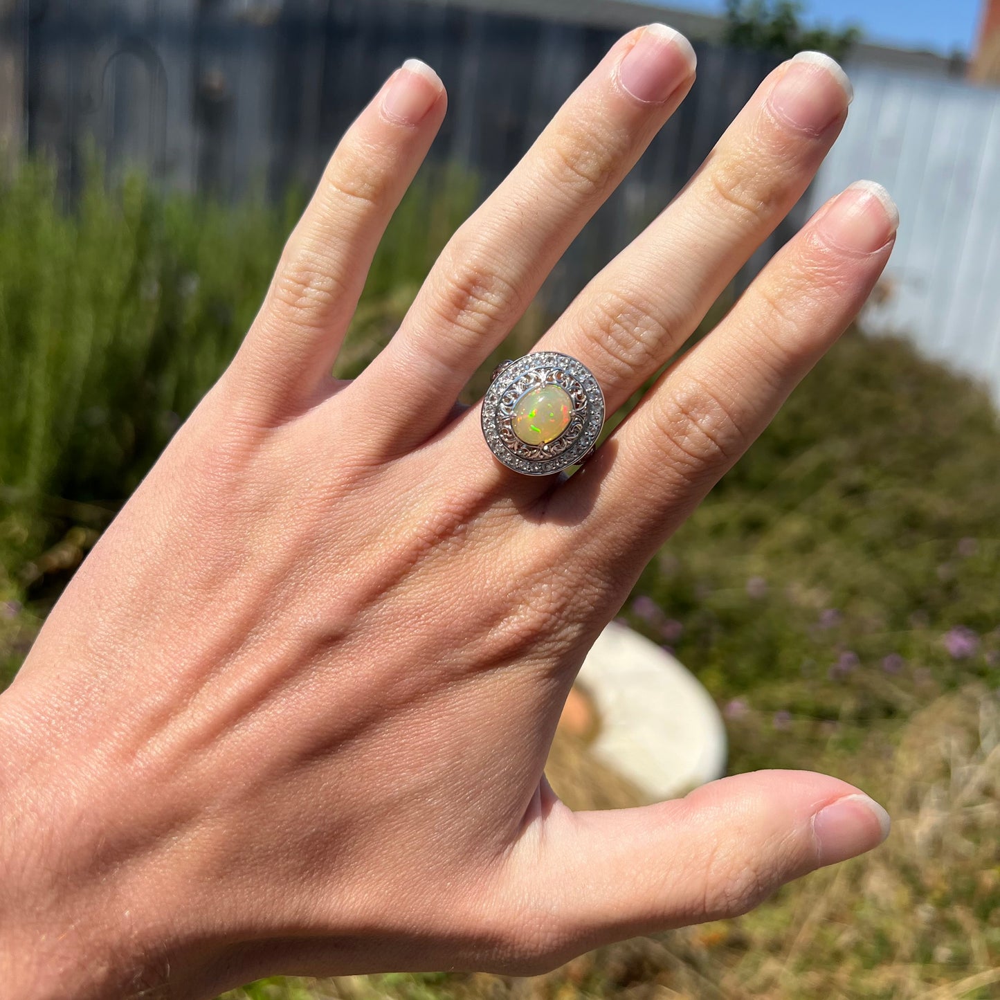 A hand wearing a large Ethiopian opal statement ring in the sunlight.