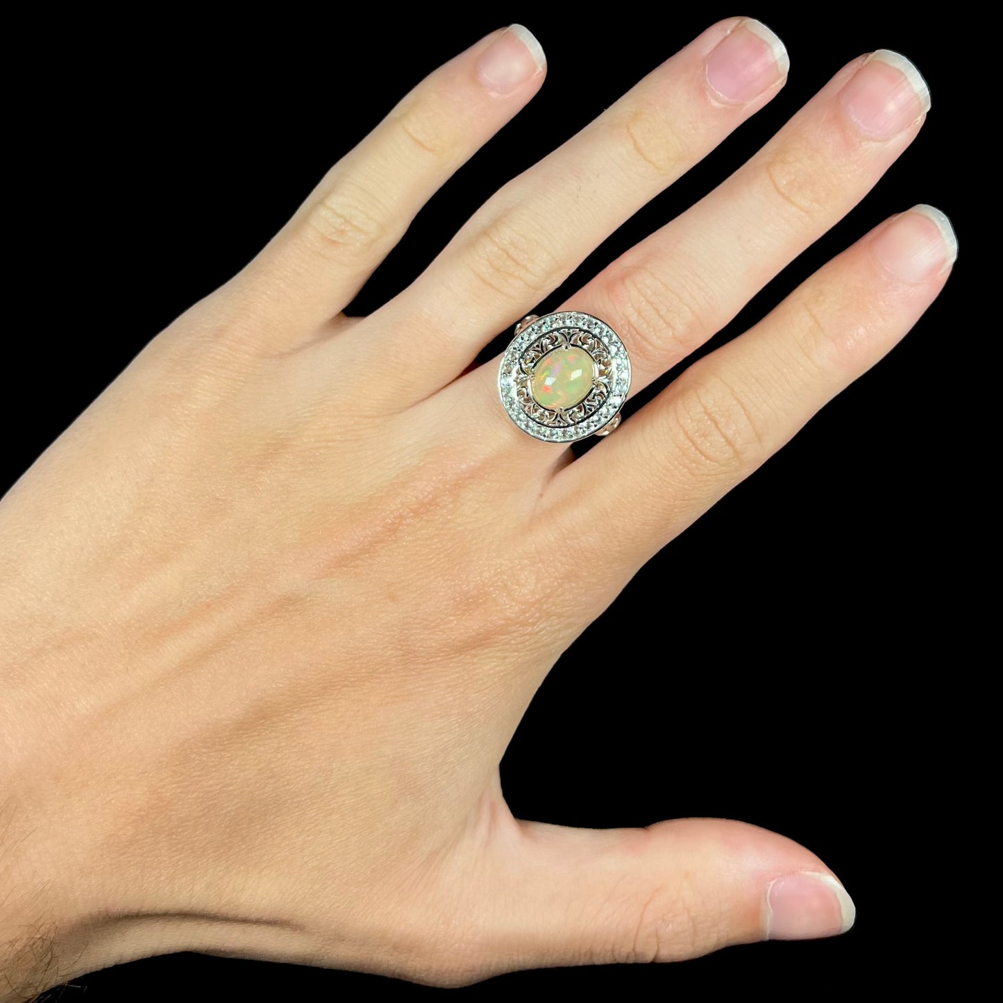 A silver Ethioipian opal statement ring with double halo worn on a hand against black background.