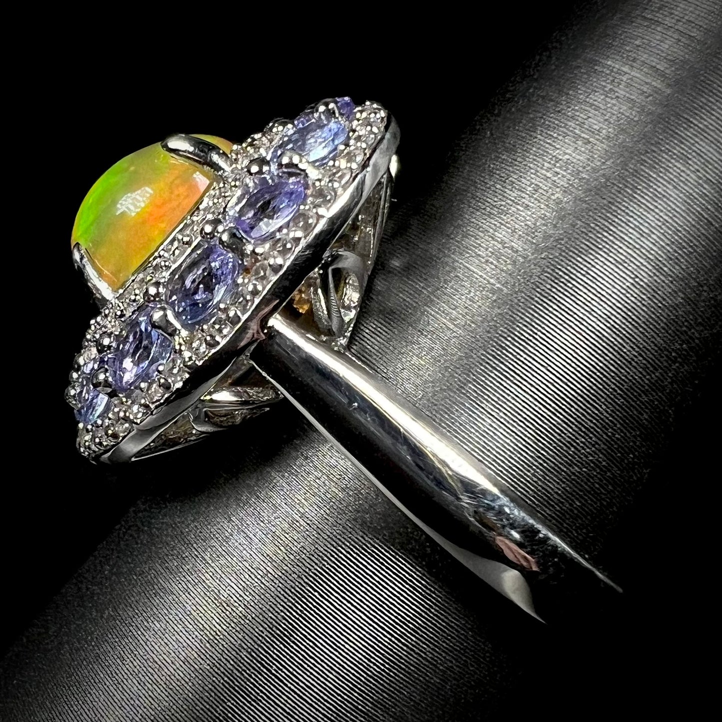 Side view of Ethiopian fire opal ring with tanzanite halo against black background.