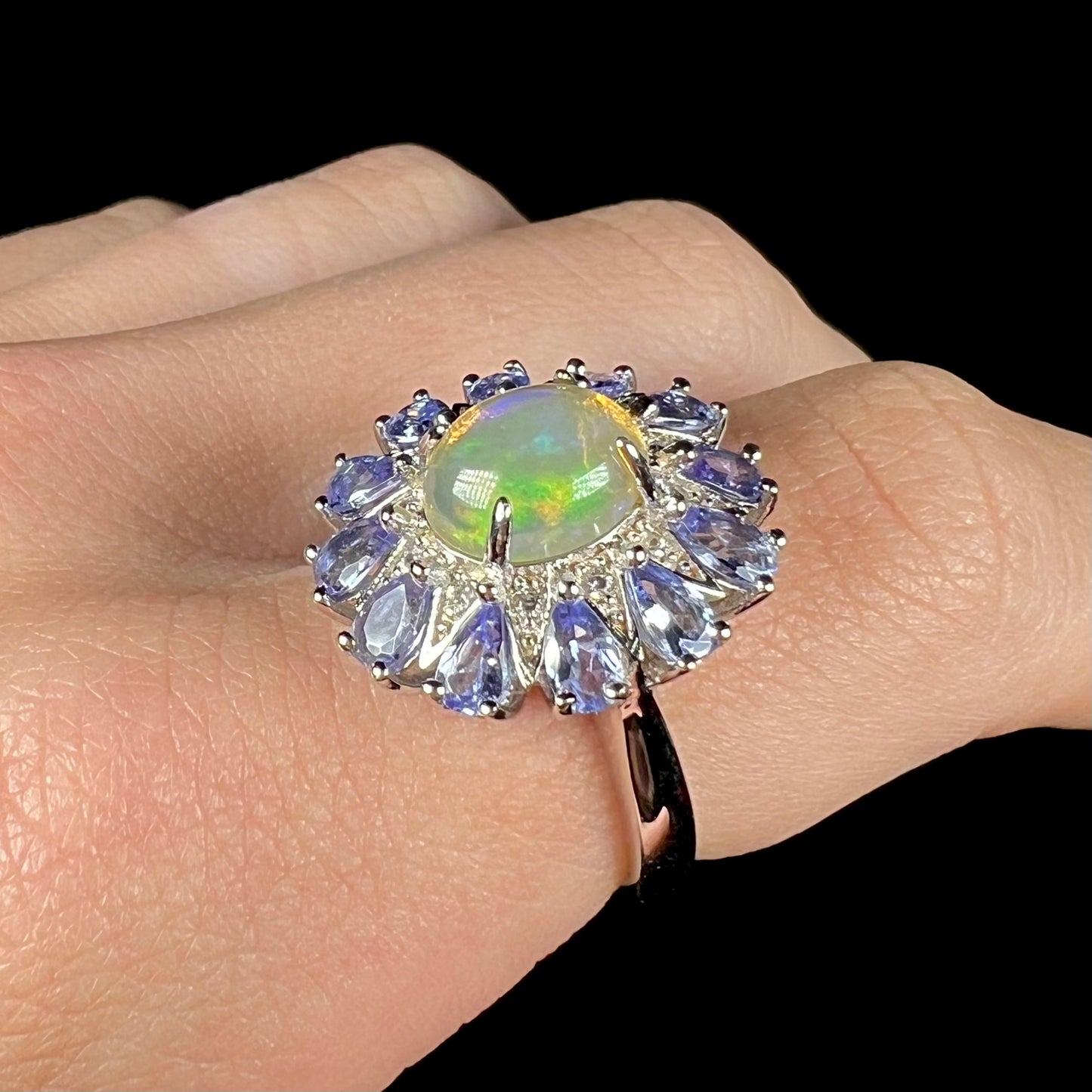 An Ethiopian opal and tanzanite-accented ring, shown at a close-up angle on a finger.