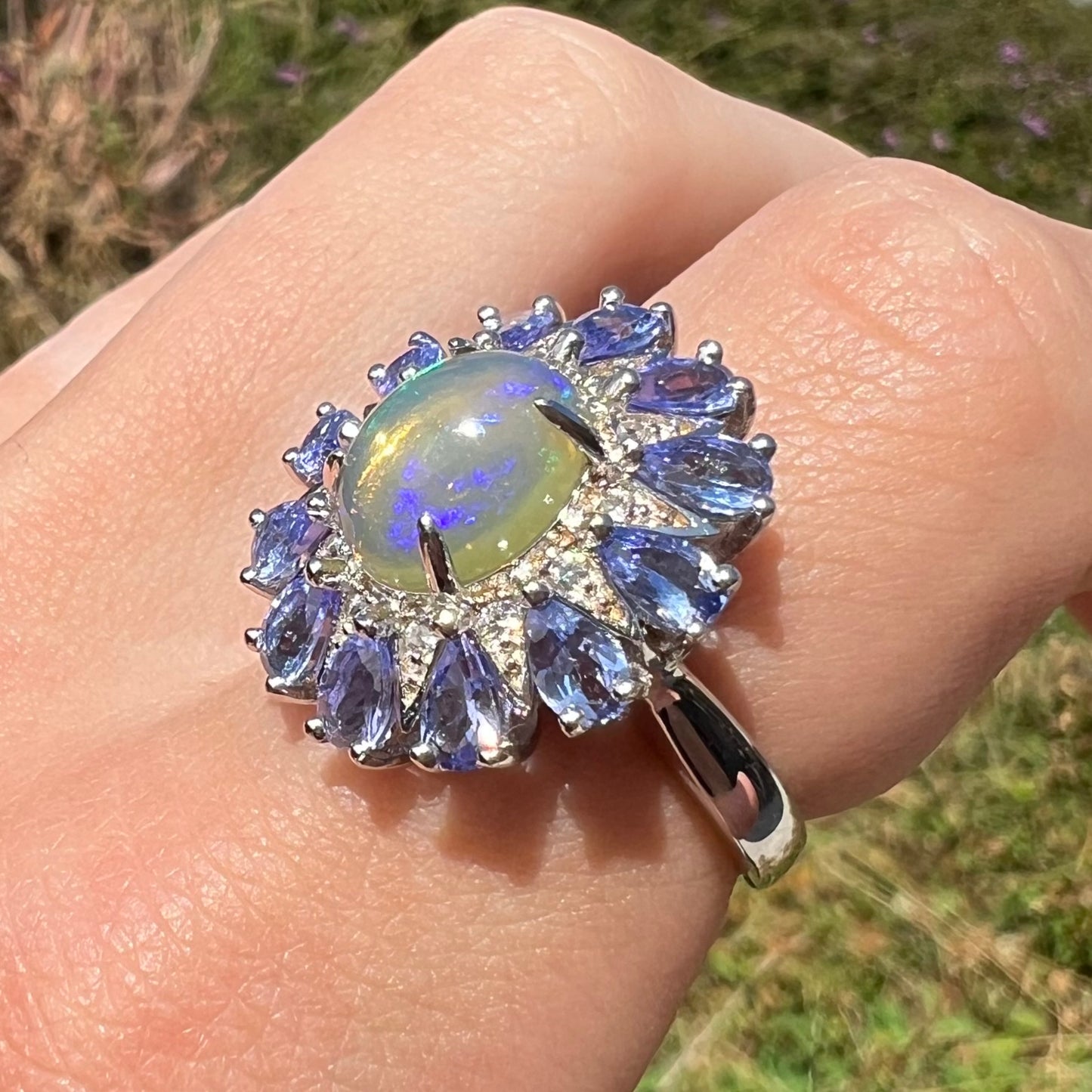 An Ethiopian opal and tanzanite starburst ring worn on a finger and shown at an angle in sunlight.