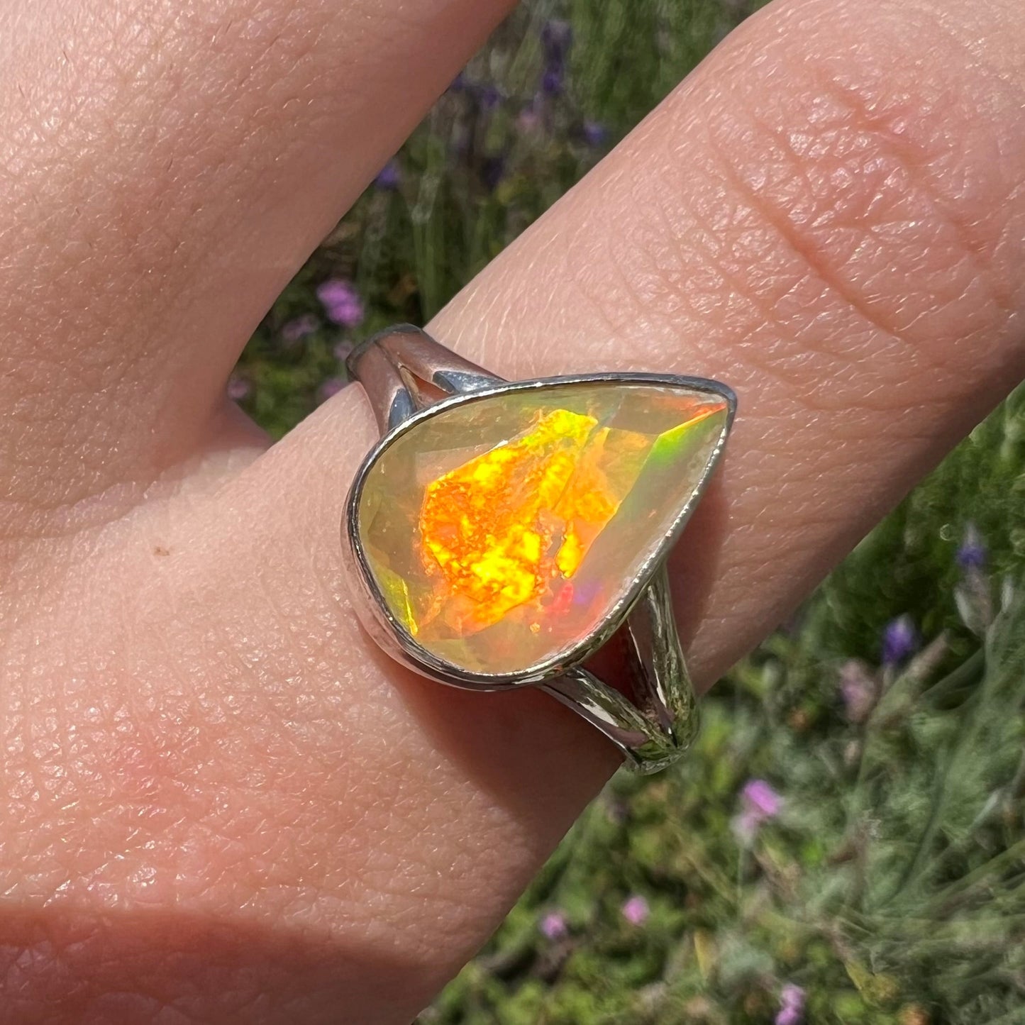 A unisex sterling silver ring set with a faceted pear shaped Ethiopian fire opal. The opal plays orange, red, and green colors.