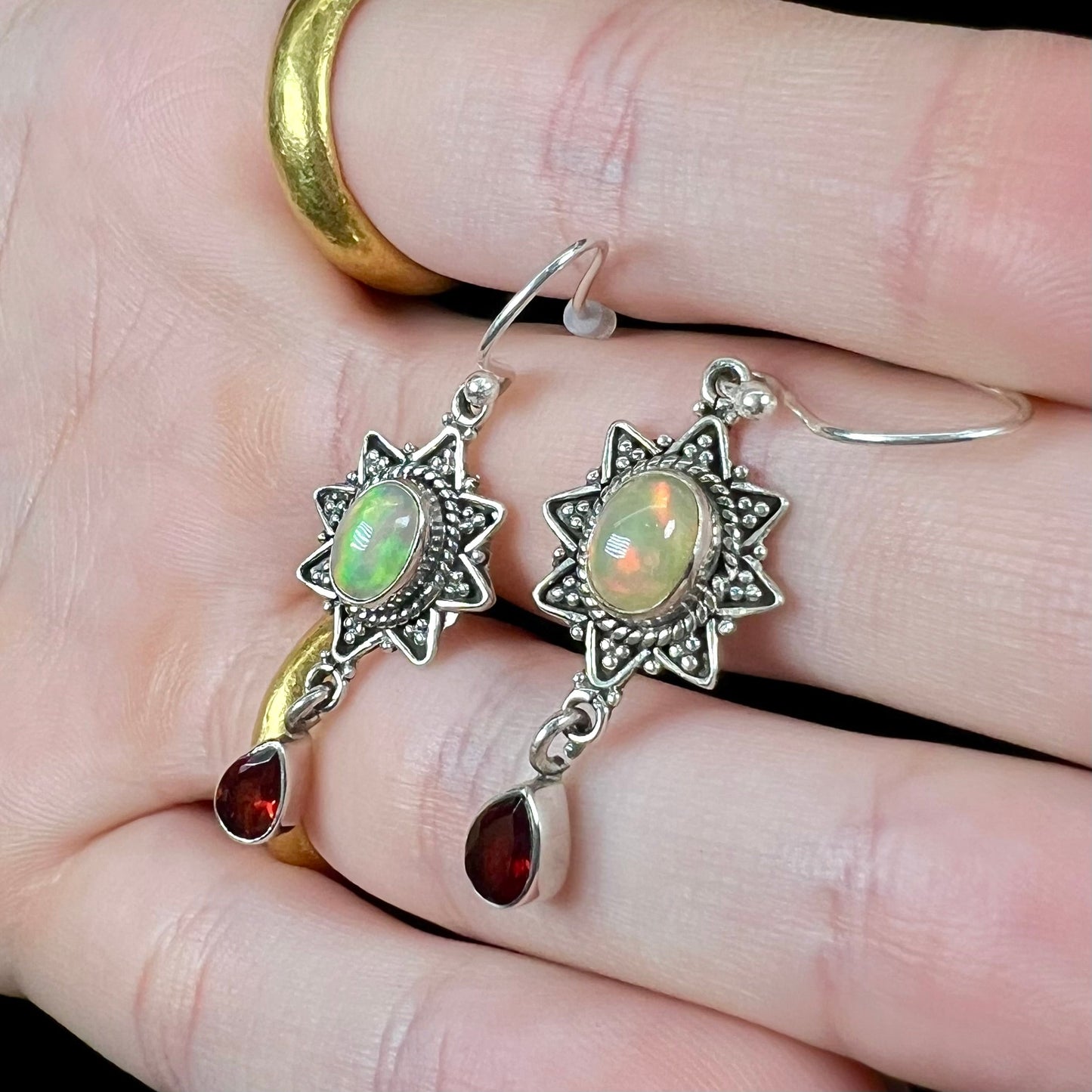 A pair of sterling silver star design dangle earrings set with Ethiopian fire opals and pear shaped red garnet accents.
