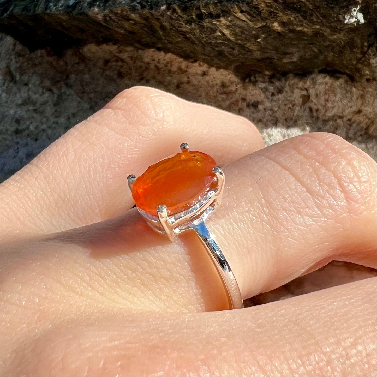 A silver solitaire ring set with a natural, faceted oval cut Mexican fire opal. The stone is a bright orange color.