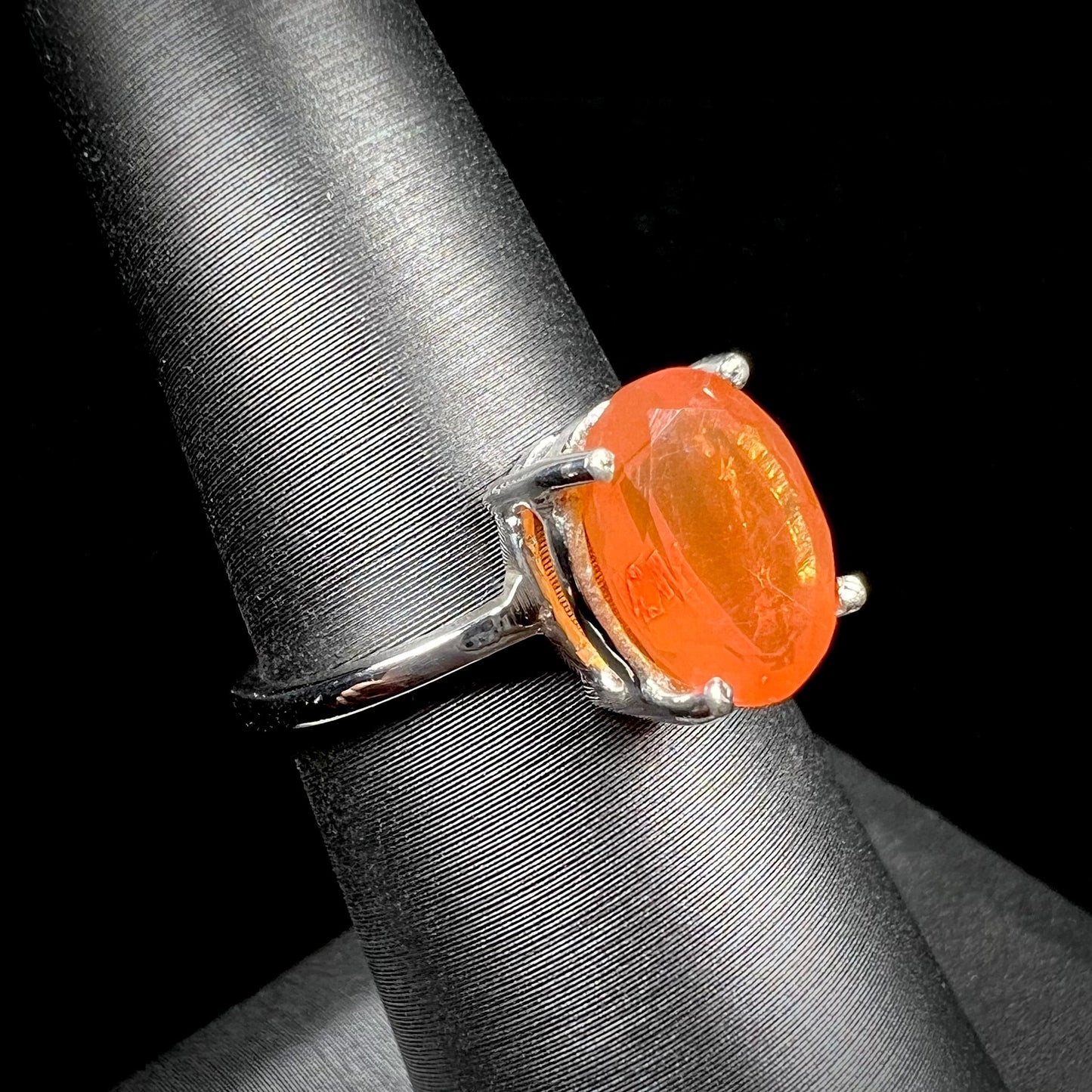 A silver solitaire ring set with a natural, faceted oval cut Mexican fire opal. The stone is a bright orange color.