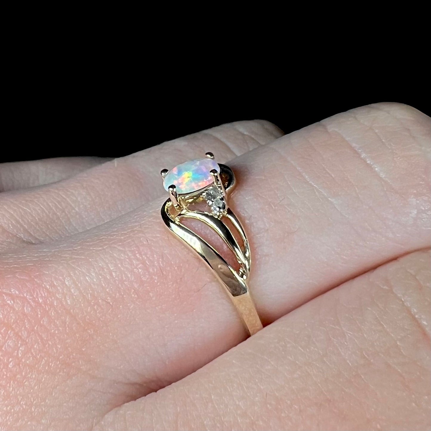 A yellow gold ring mounted with two diamond accents and an oval cut lab created opal. The opal has bright red colors.