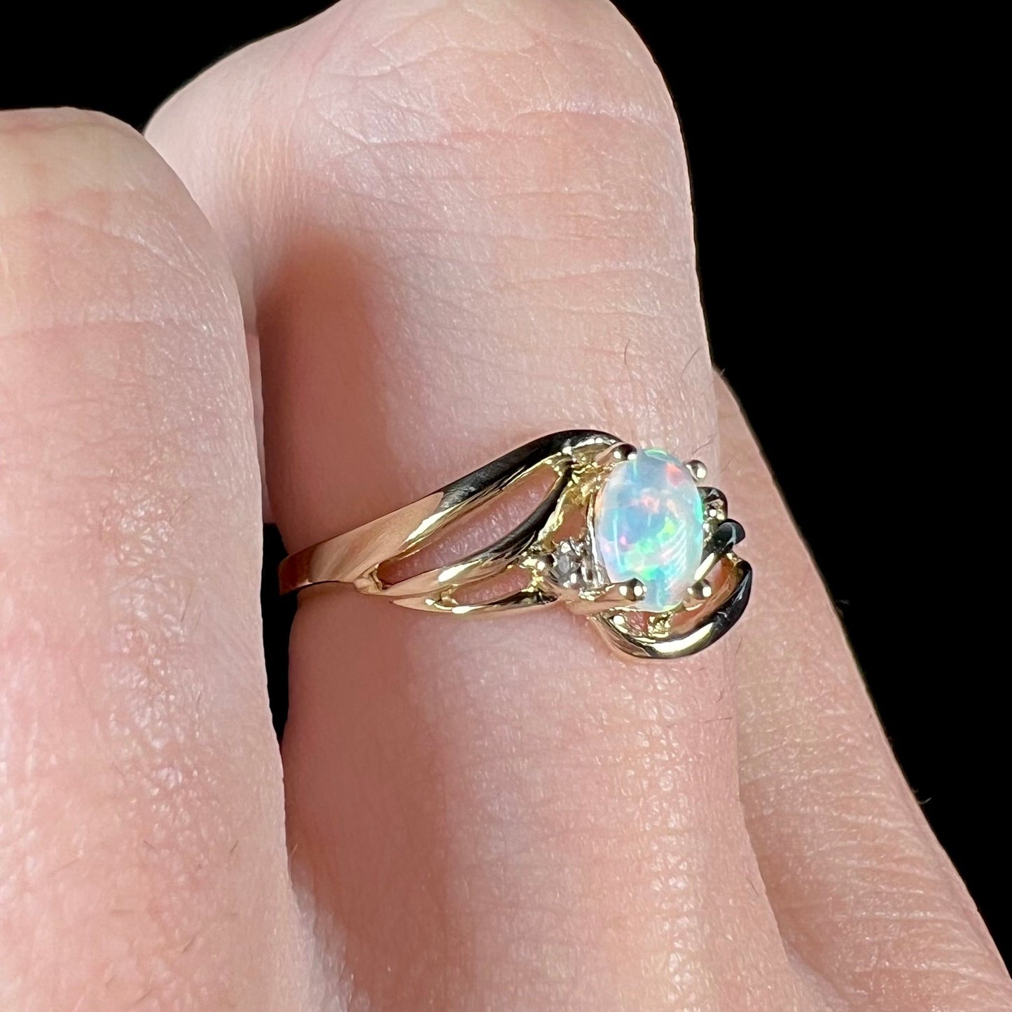 A yellow gold ring mounted with two diamond accents and an oval cut lab created opal. The opal has bright red colors.