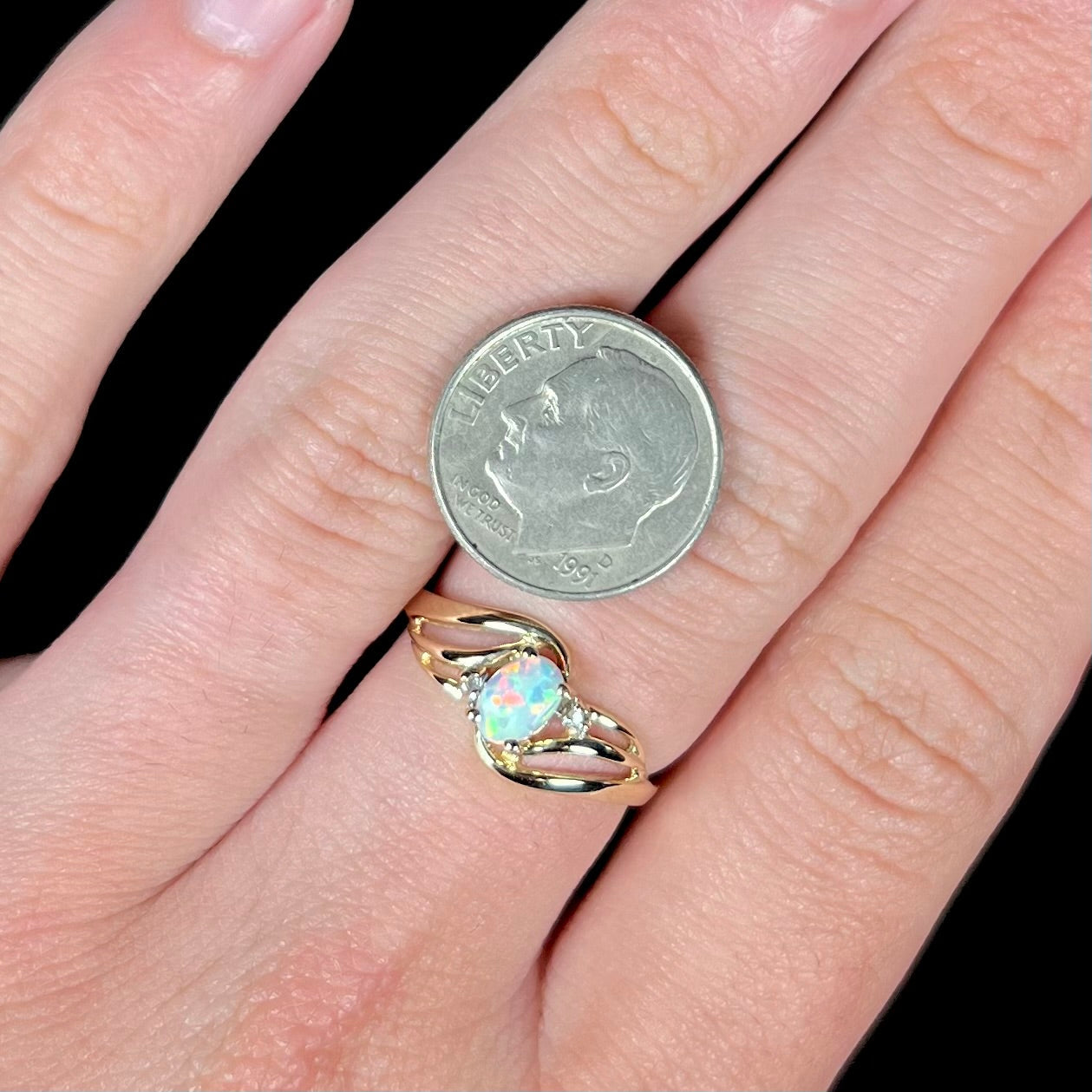 A yellow gold ring mounted with two diamond accents and an oval cut lab created opal. The opal has bright red colors.