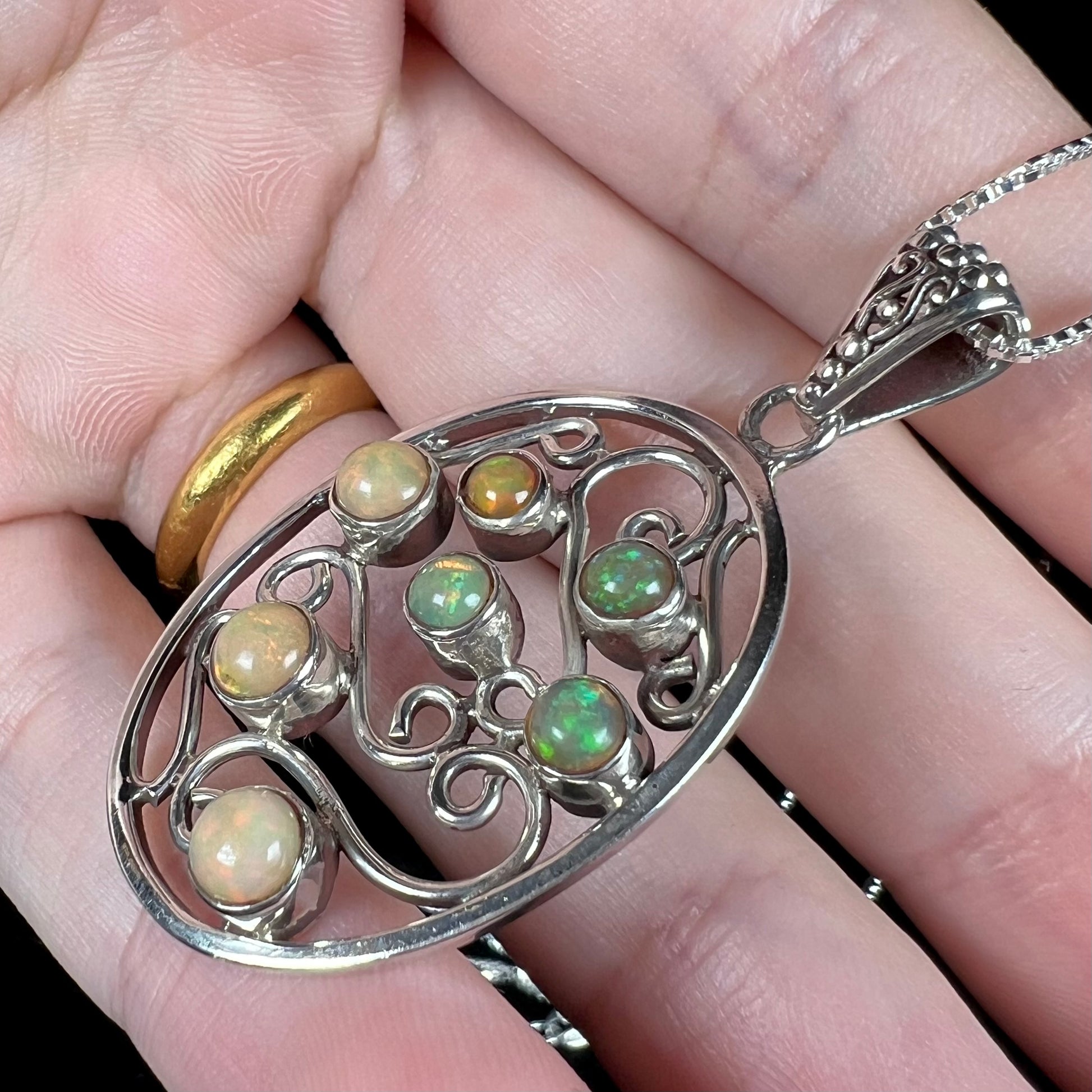 A sterling silver Ethiopian opal filigree necklace shown at an angle in a hand against a black backdrop.