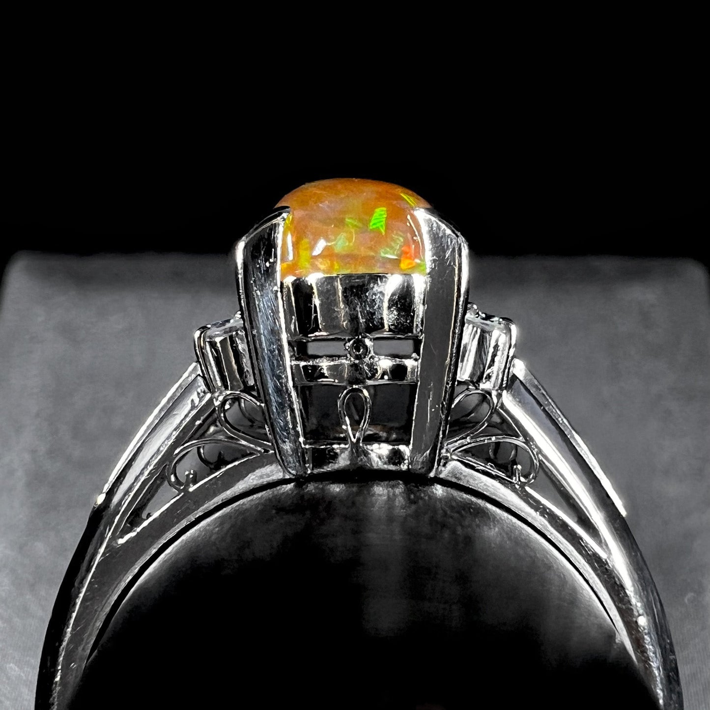 A platinum filigree and diamond-accented Mexican fire opal ring. The opal is orange with green fire.