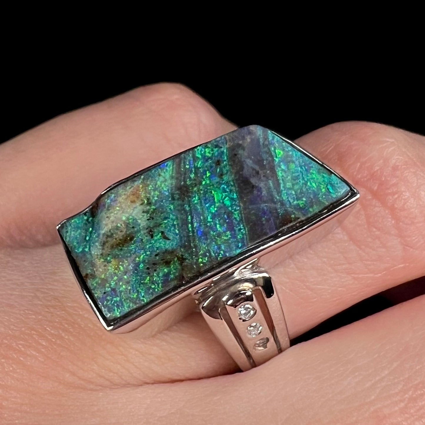 Angled close-up of a fine Australian boulder opal and diamond ring in platinum, worn on a finger.