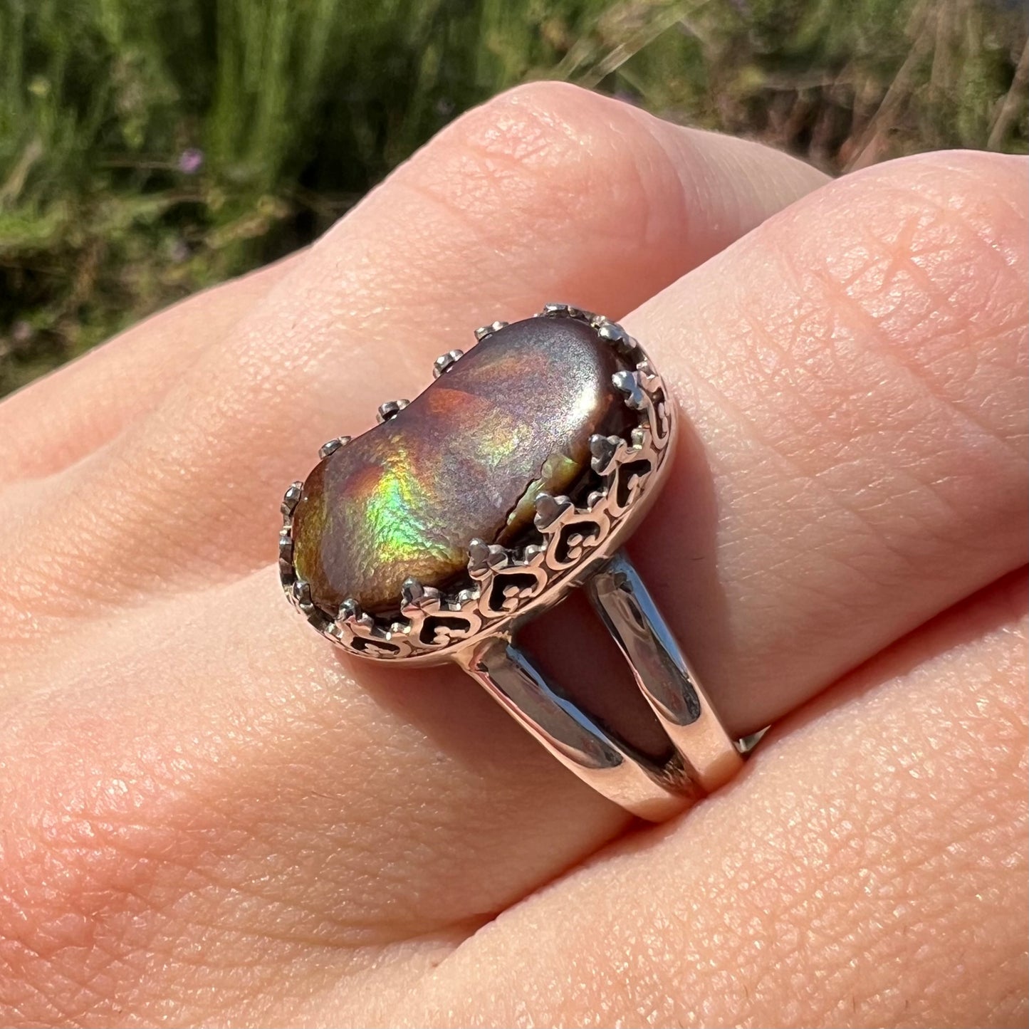 A fire agate ring with a crown design worn on finger at an angle in sunlight, highlighting a crack in the stone.