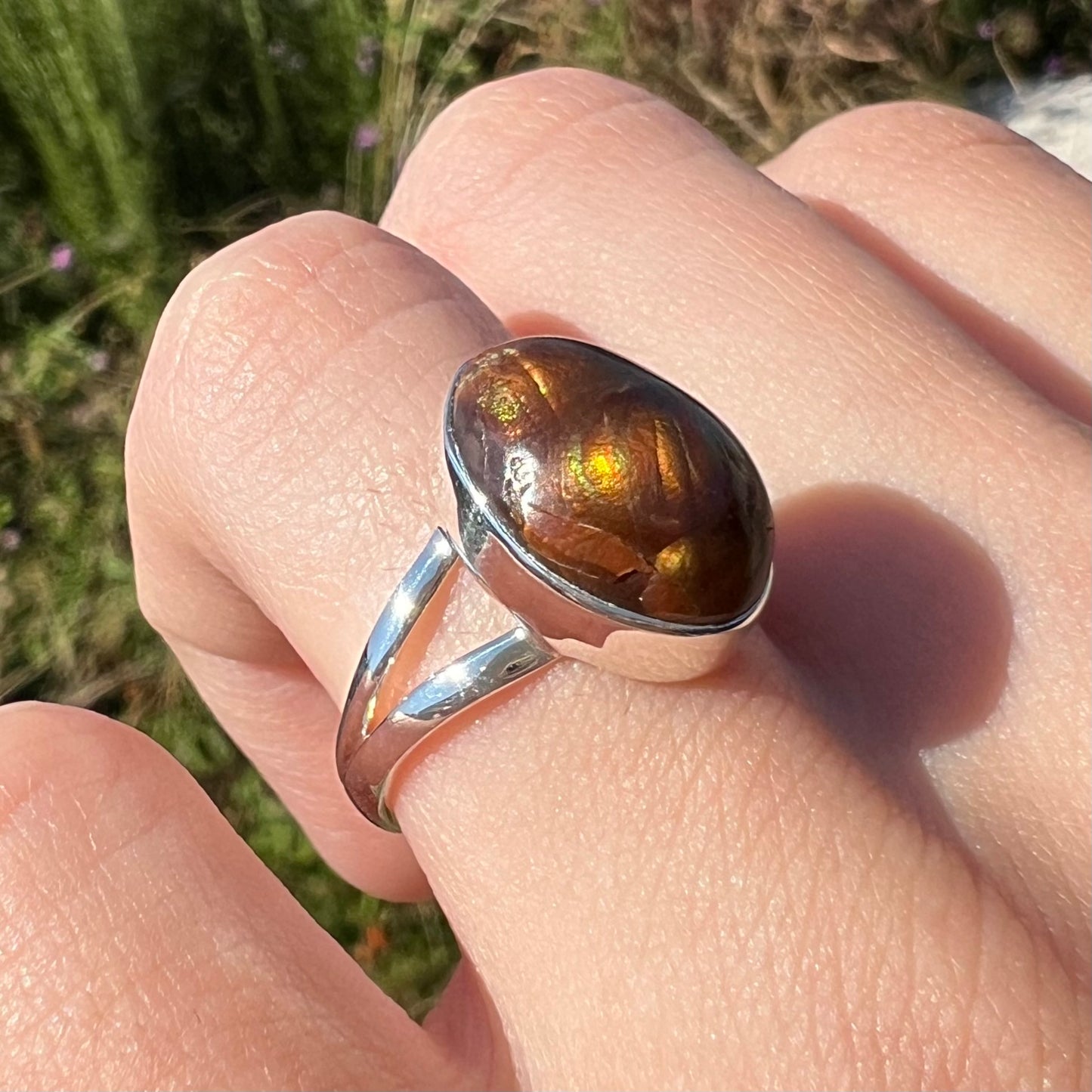 Angled close-up view of a sterling silver Mexican fire agate ring with a split shank worn on finger.