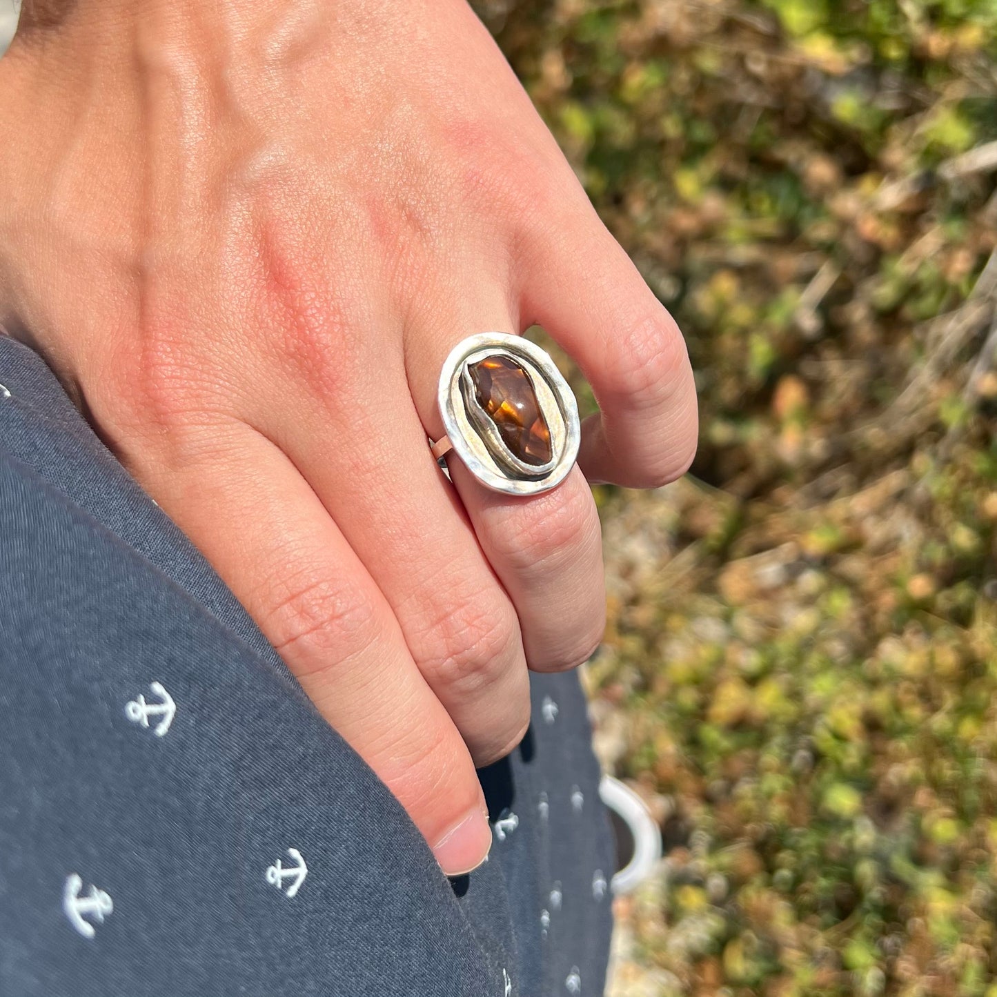 Hand wearing a handmade sterling silver fire agate ring in the sunlight while resting on the model's hip.