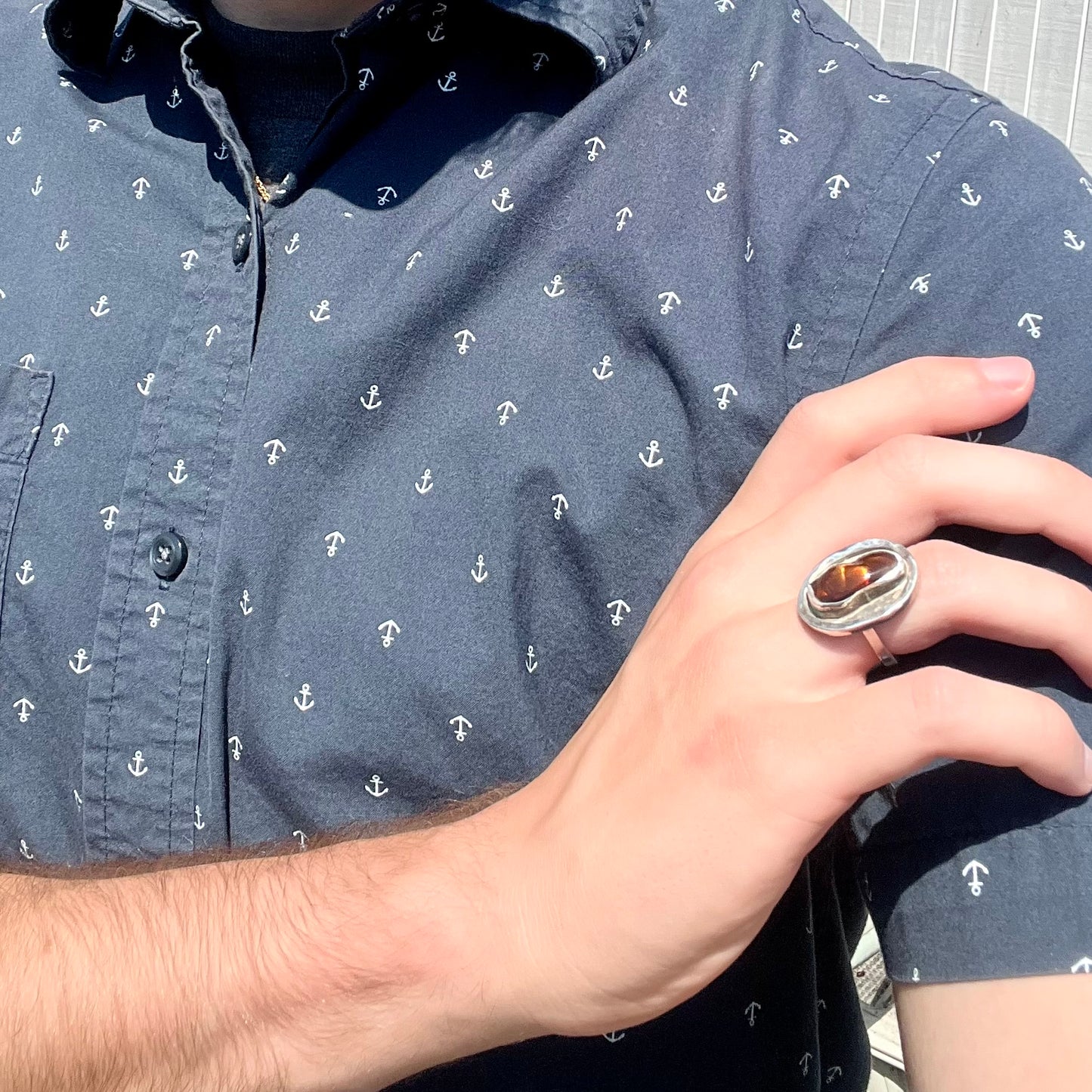 A handmade sterling silver fire agate ring worn on a model's hand as the hand rests on the model's opposing shoulder.