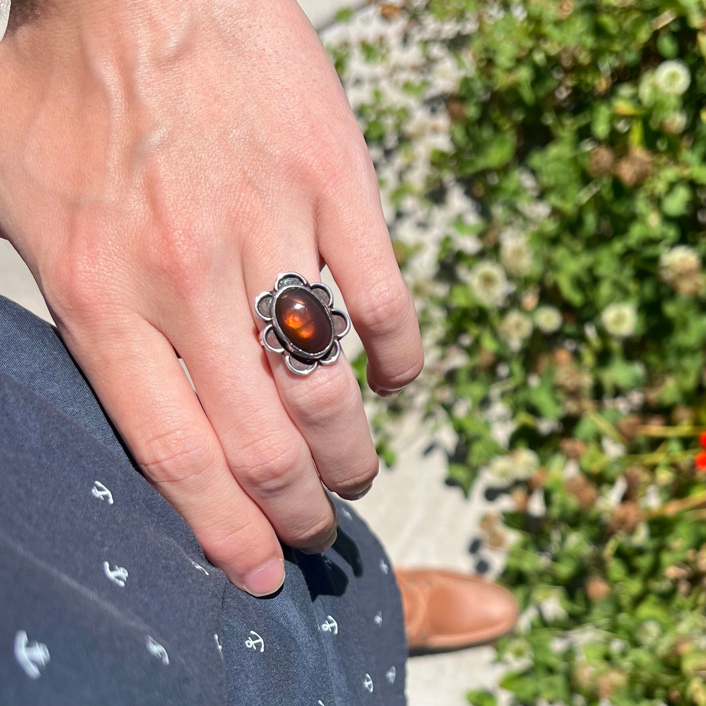 Ring worn on hip in sunlit garden, red-orange iridescence glowing.