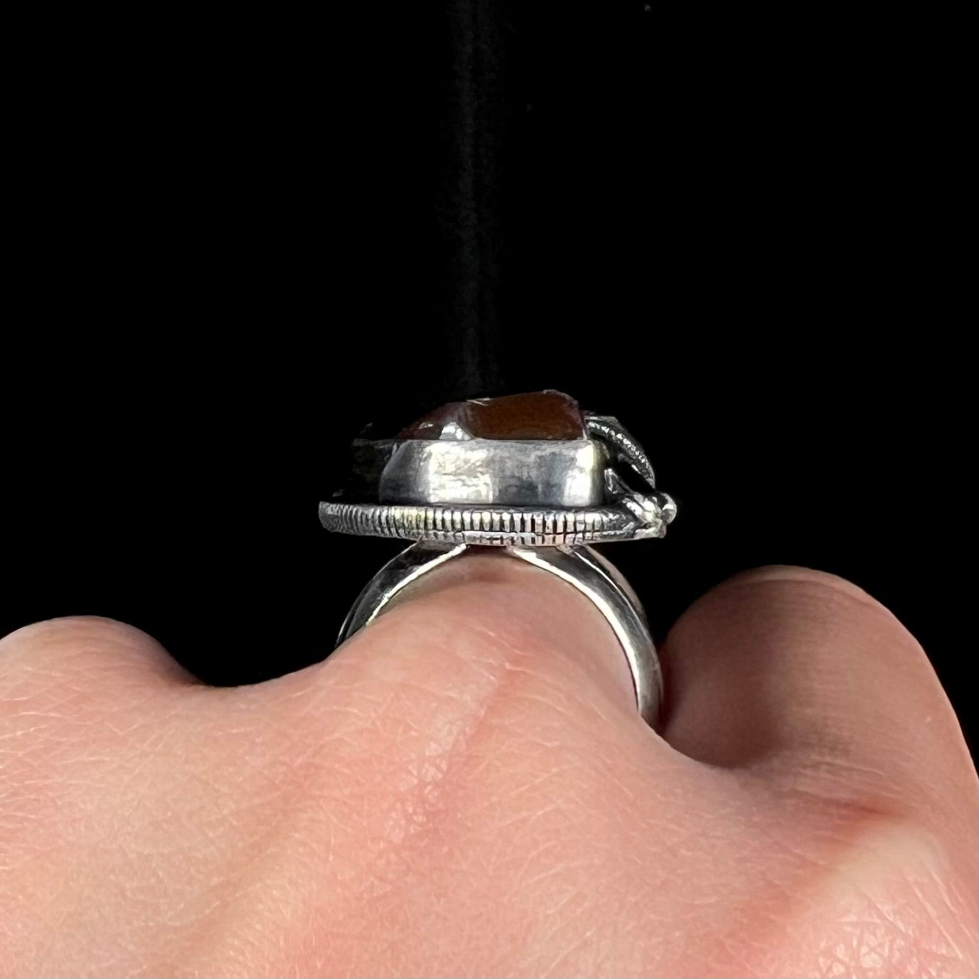 A men's silver, Southwest-style fire agate ring worn on a hand and shown by the side gallery profile view.