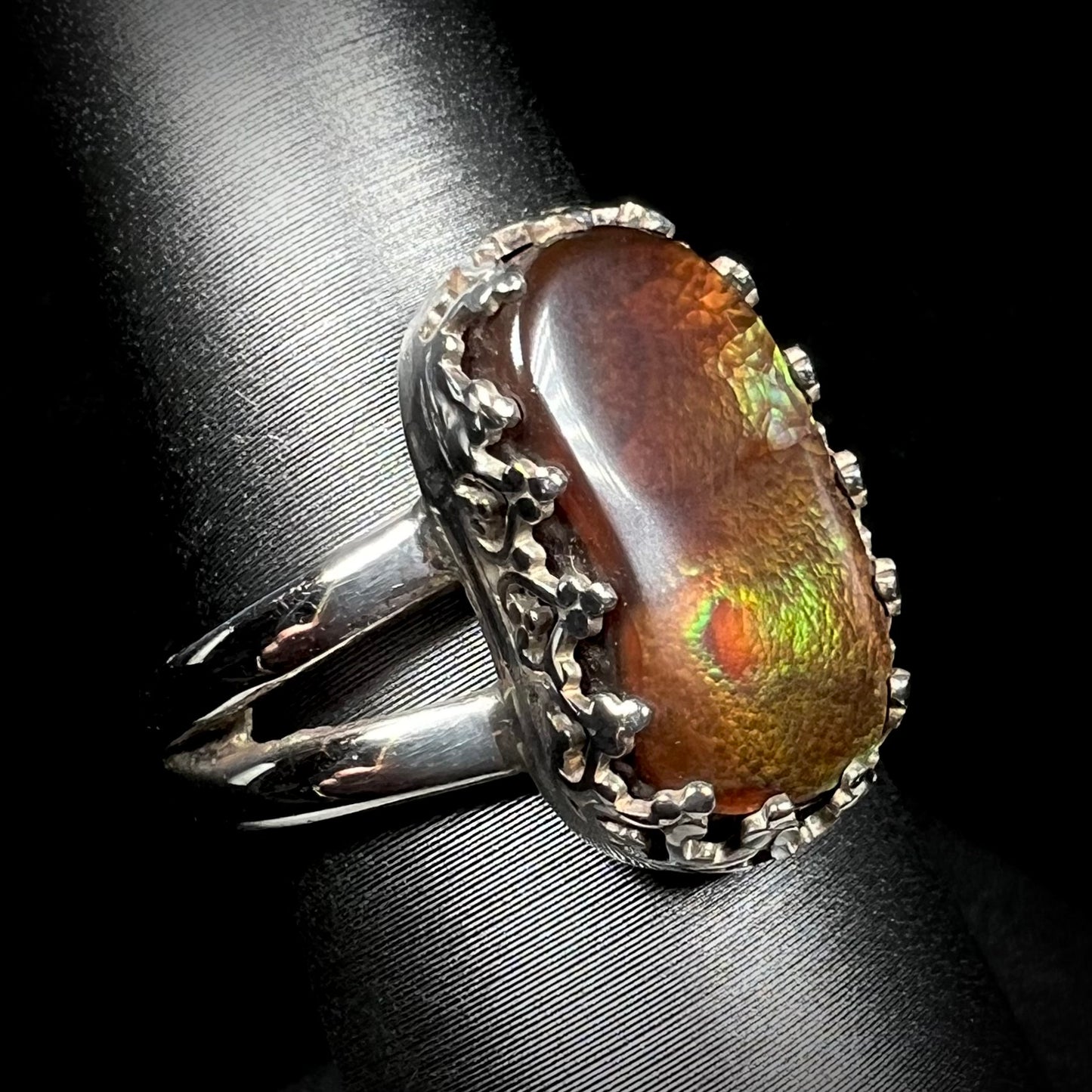 A fire agate ring with silver crown-design prongs and a split shank shown from an angled view.