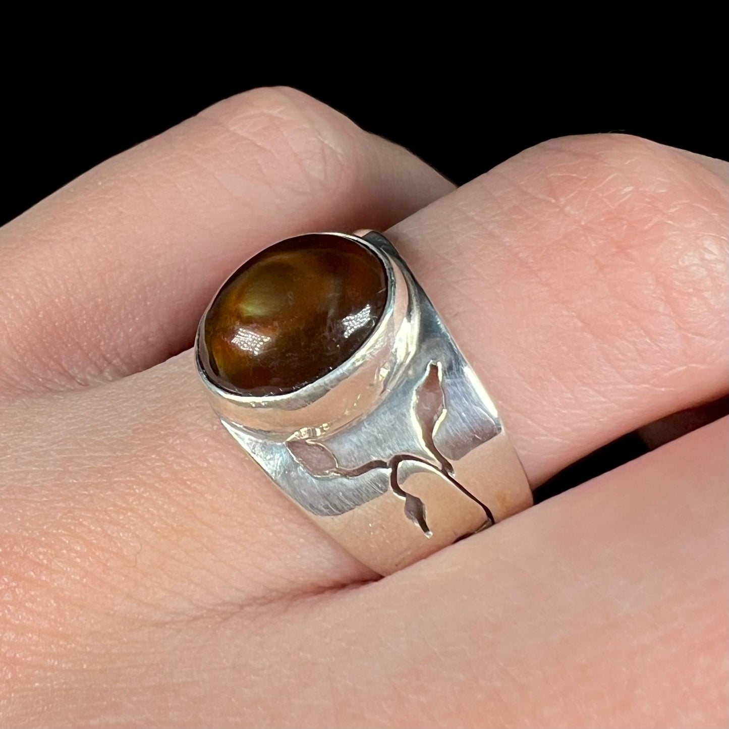 A sterling silver fire agate ring, worn on a finger, shown close-up at an angle against a black background.