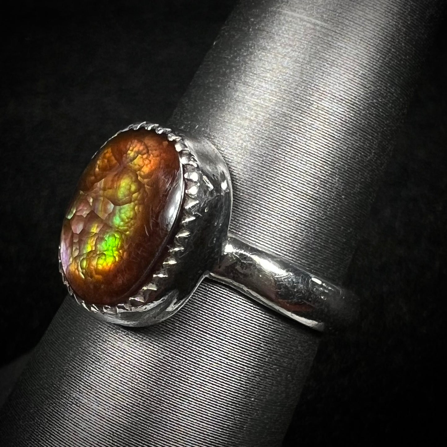 A fire agate solitaire ring in sterling silver, shown from an angled view with green and purple iridescence.