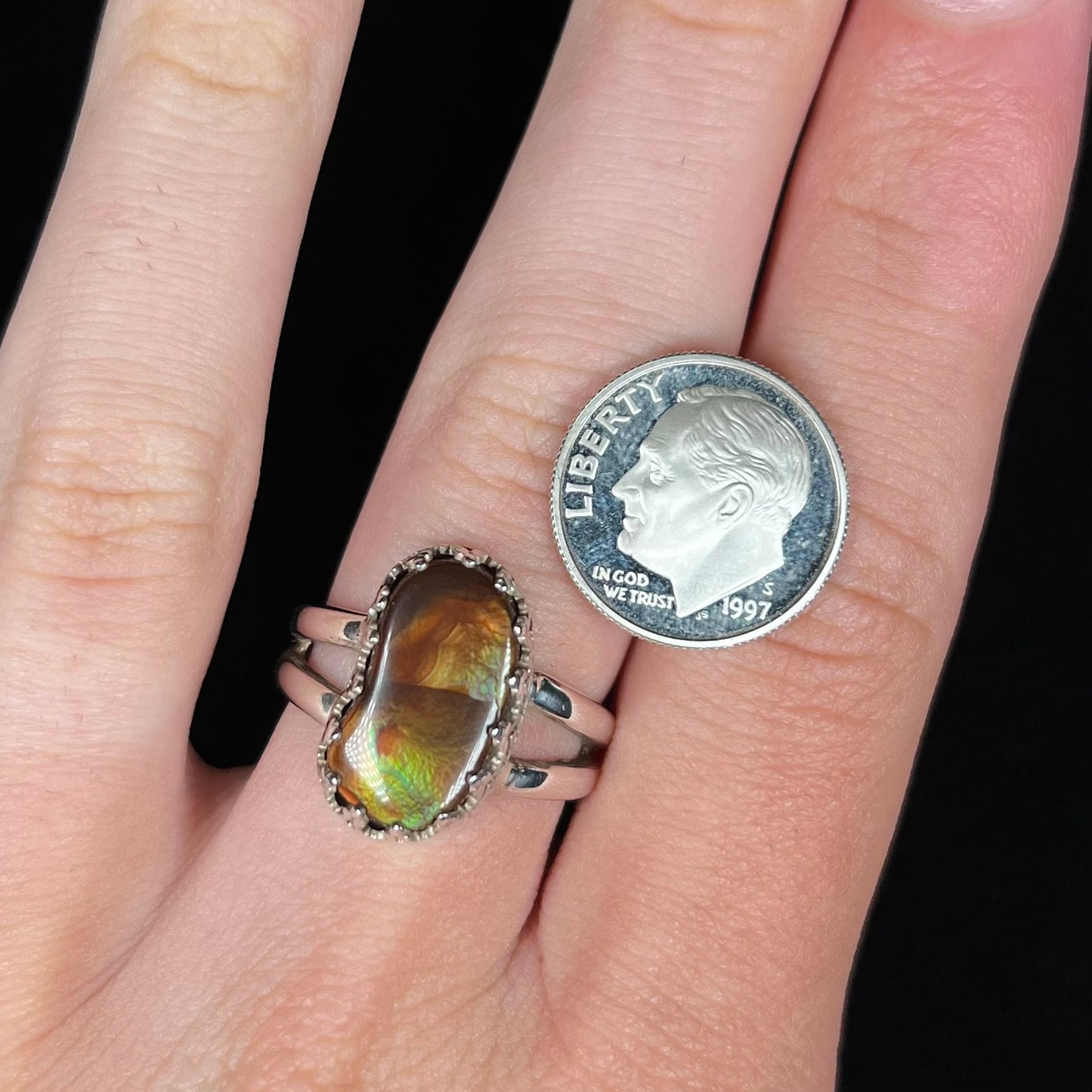Hand wearing a freeform shaped fire agate solitaire ring next to a dime coin for scale.
