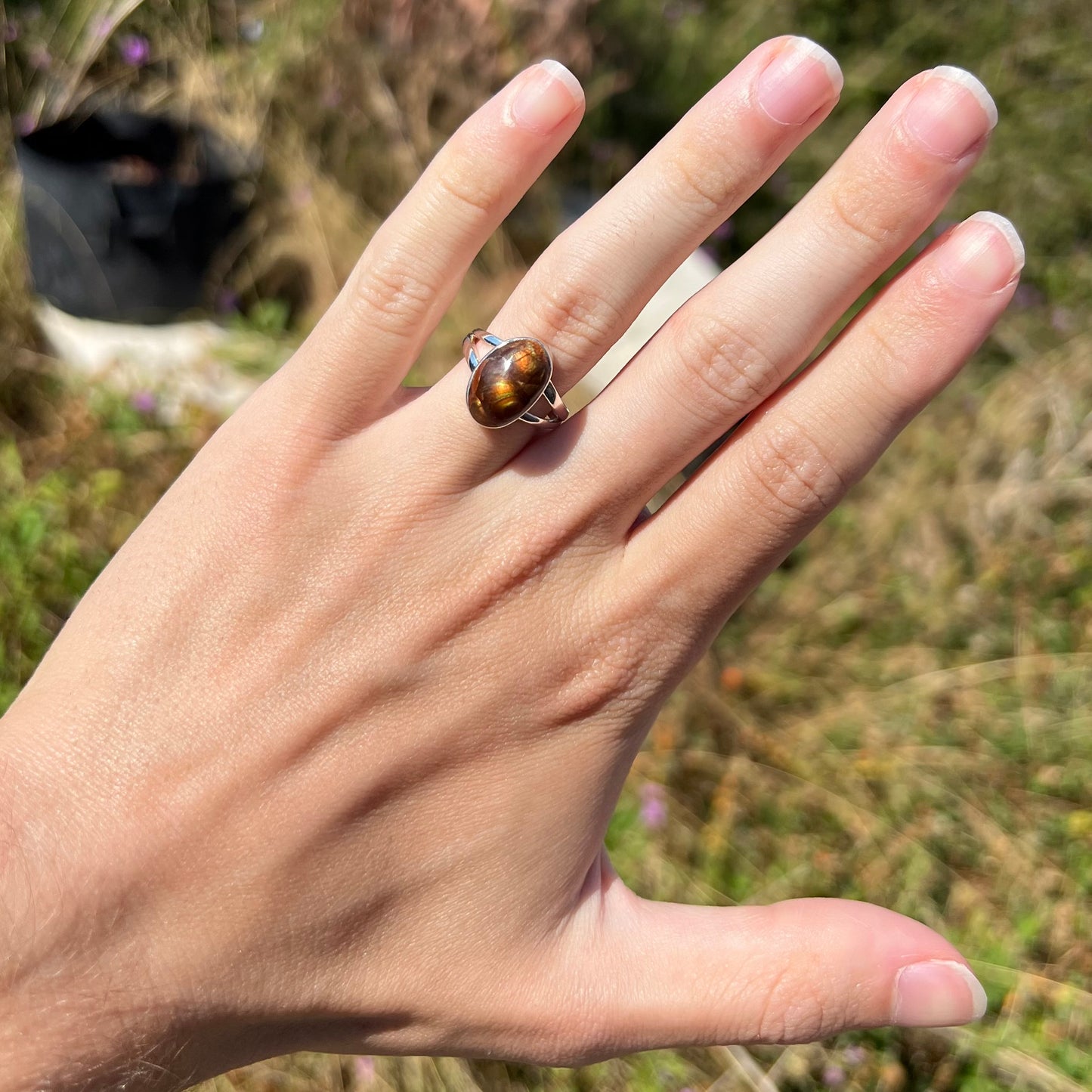 A sterling silver Mexican fire agate ring with a split shank worn on a hand in the sunlight.