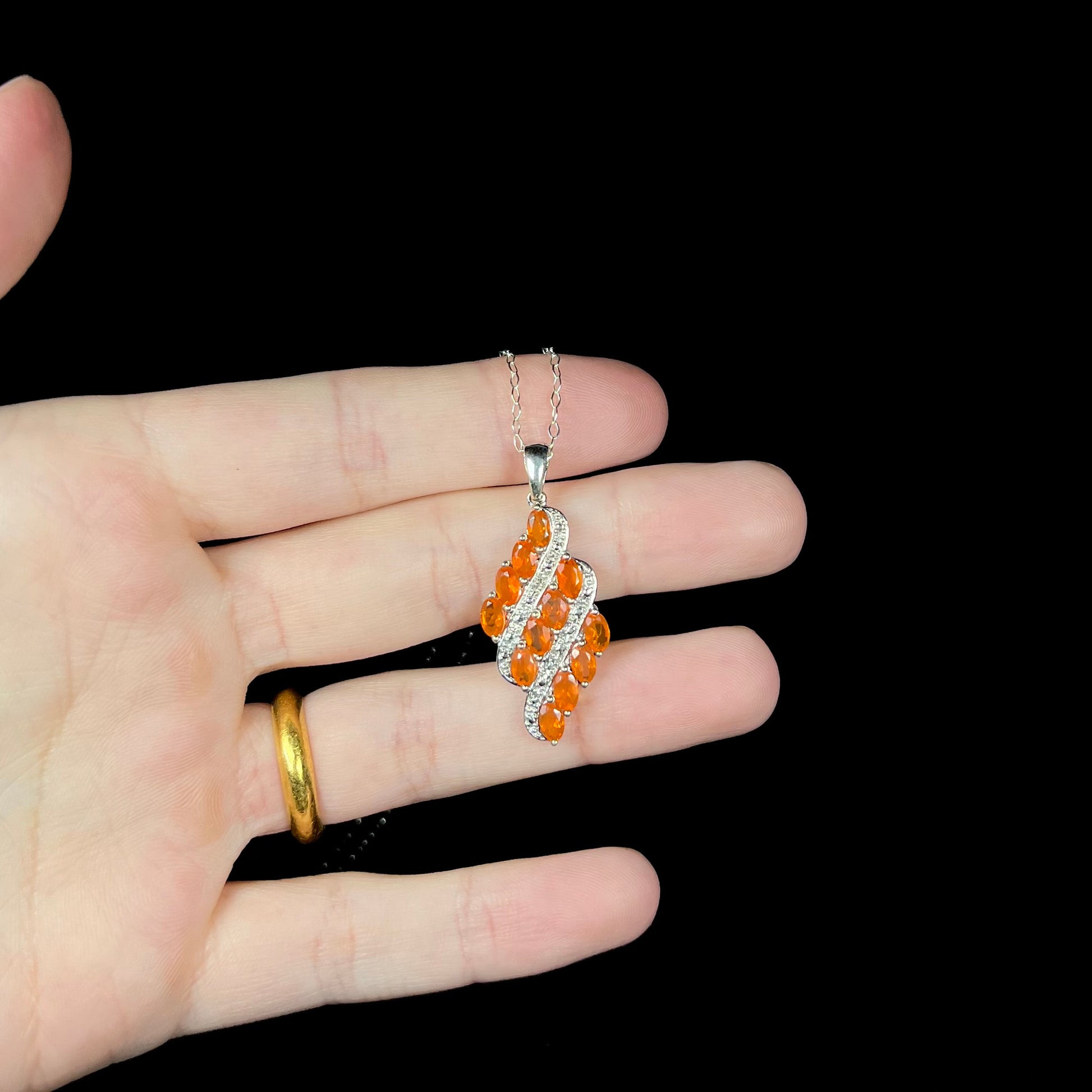 A sterling silver Mexican fire opal necklace featuring a cluster of faceted orange fire opals, held in a hand.