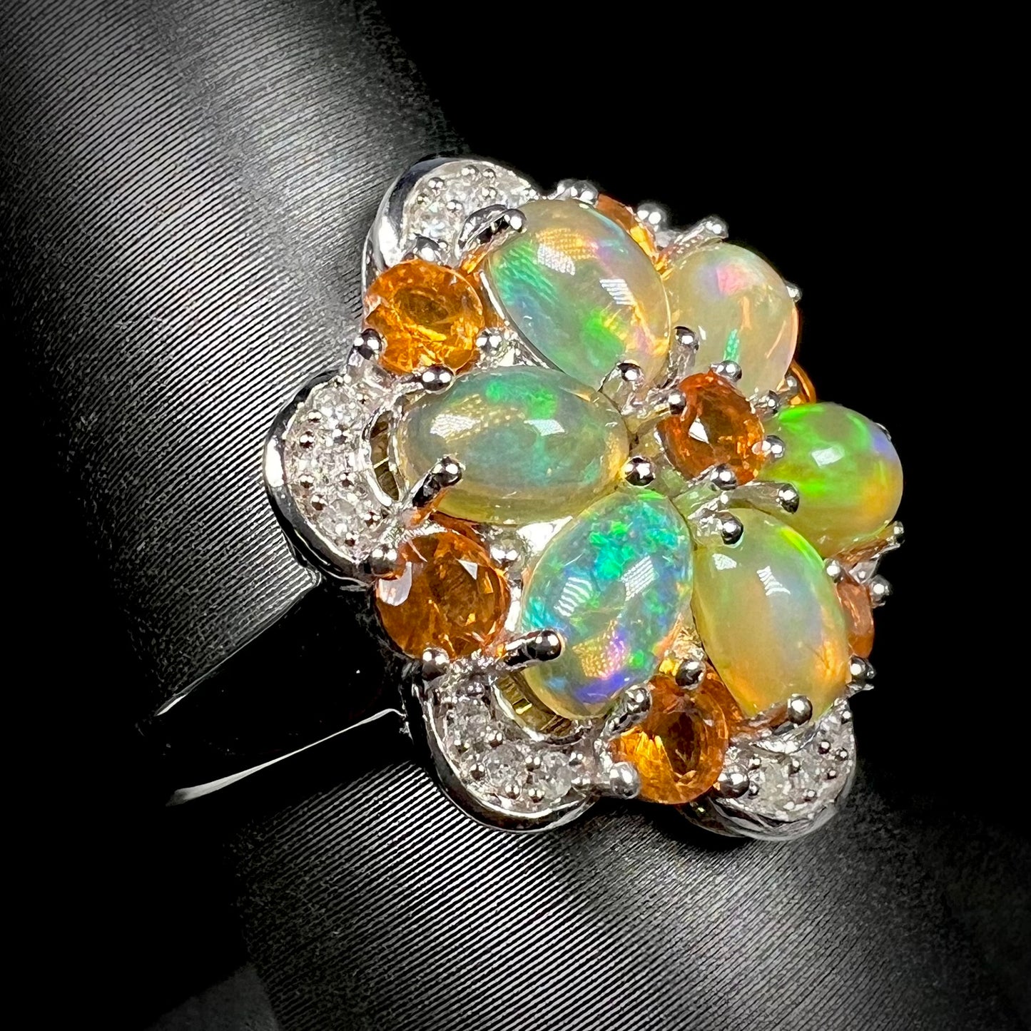 A fire opal and diamond cluster ring that resembles a flower, shown at an angle against a black background.