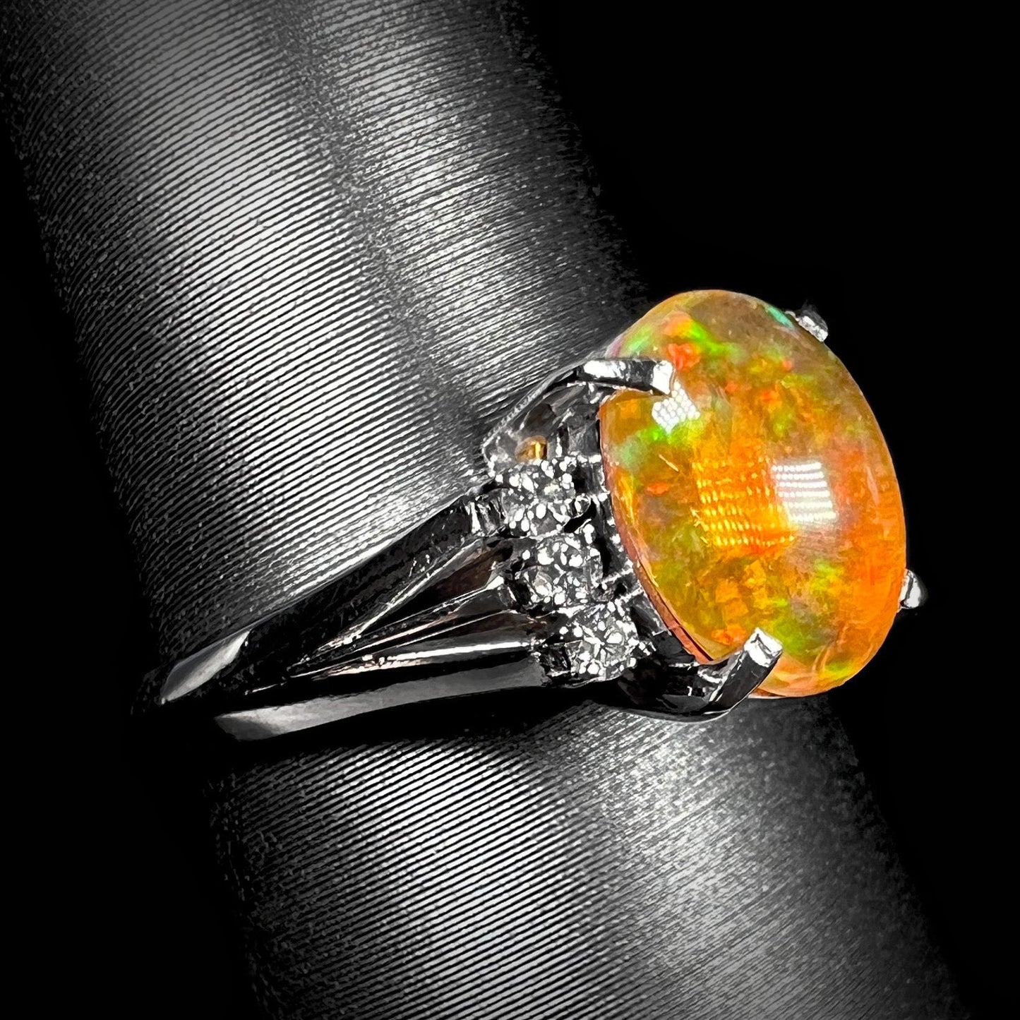 A platinum filigree and diamond-accented Mexican fire opal ring. The opal is orange with green fire.