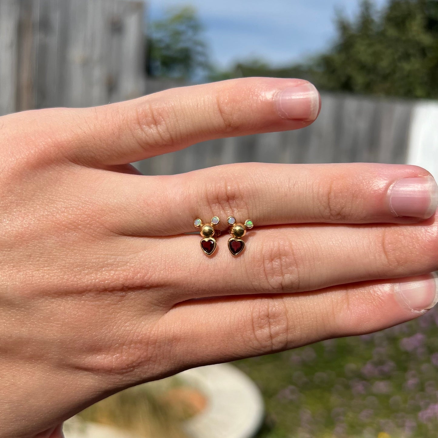 A pair of 18 karat yellow gold stud earrings set with two round fire opals and heart shaped garnets.